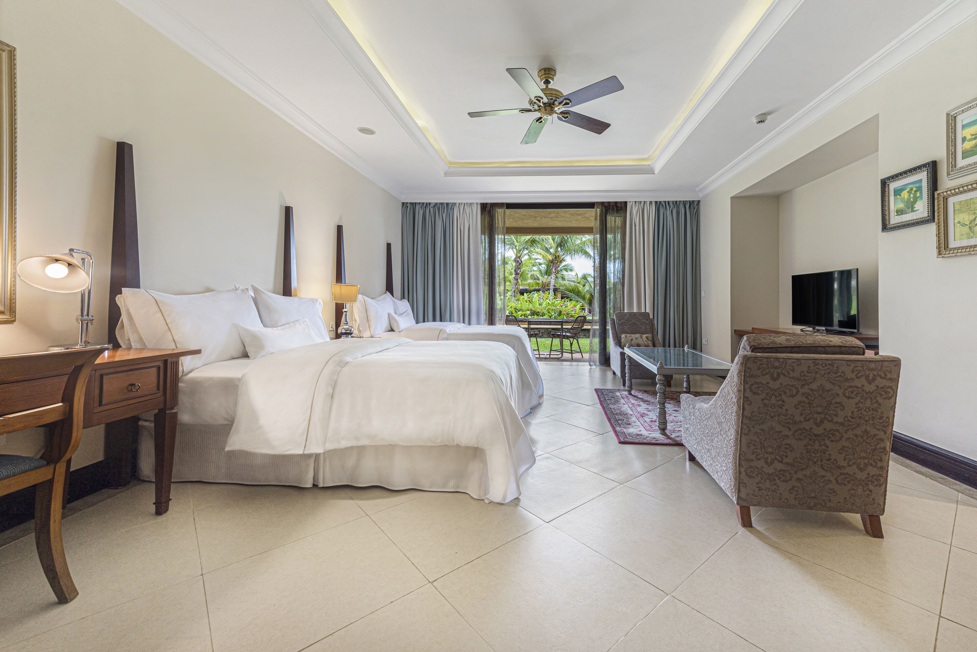 A hotel room with a bed, desk, chair, television, and a balcony with curtains.