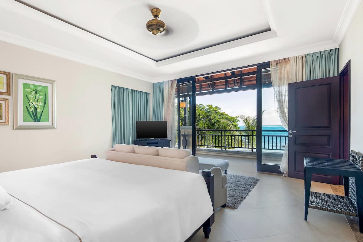 Quarto com cama grande, sofá, televis ão e varanda com vista.