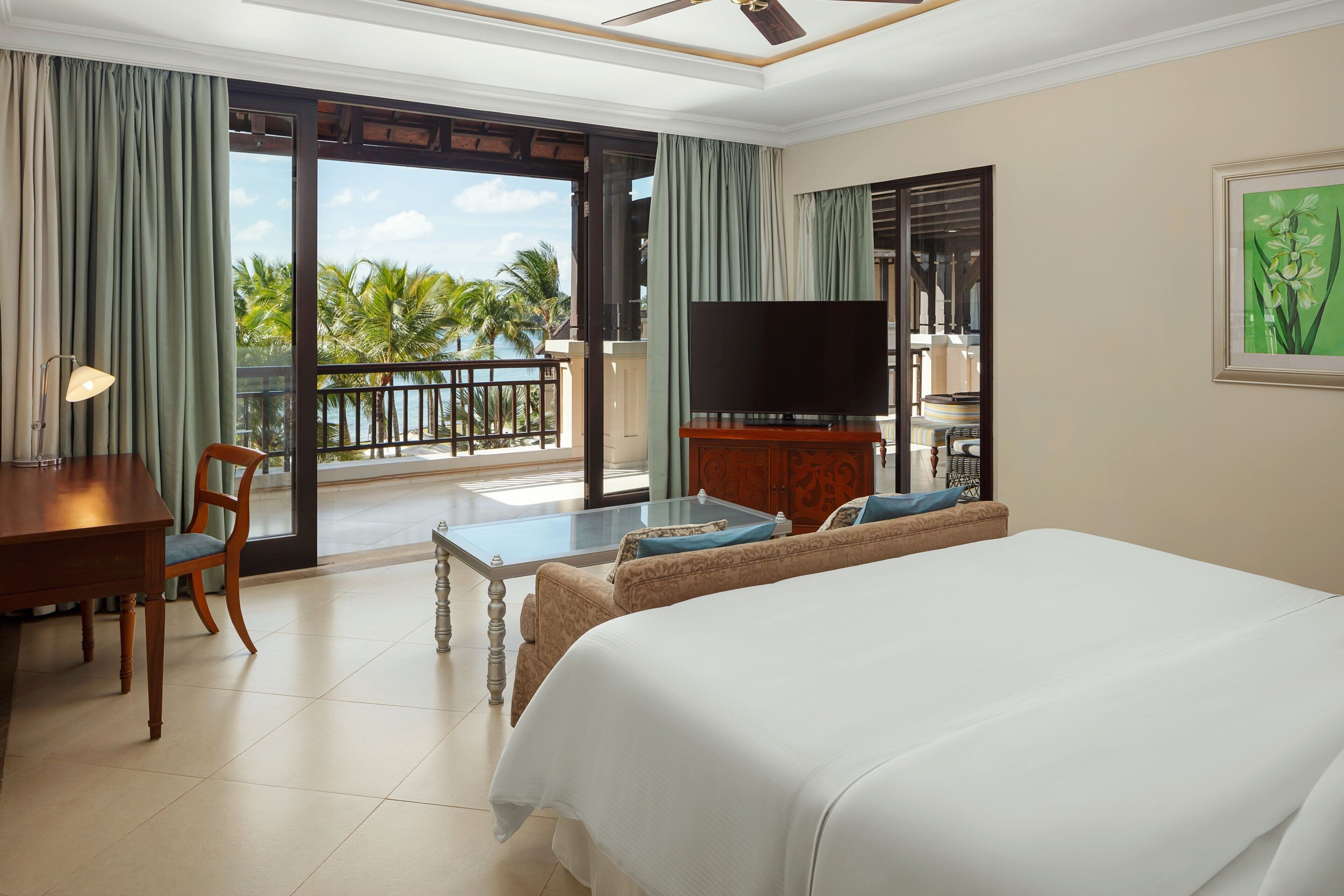 A hotel room with a balcony, a bed, a desk, and a television.