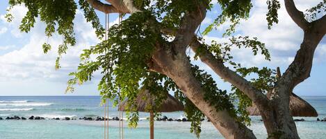 A beach scene with a swing, a thatched-roof structure, and a wooden chair.