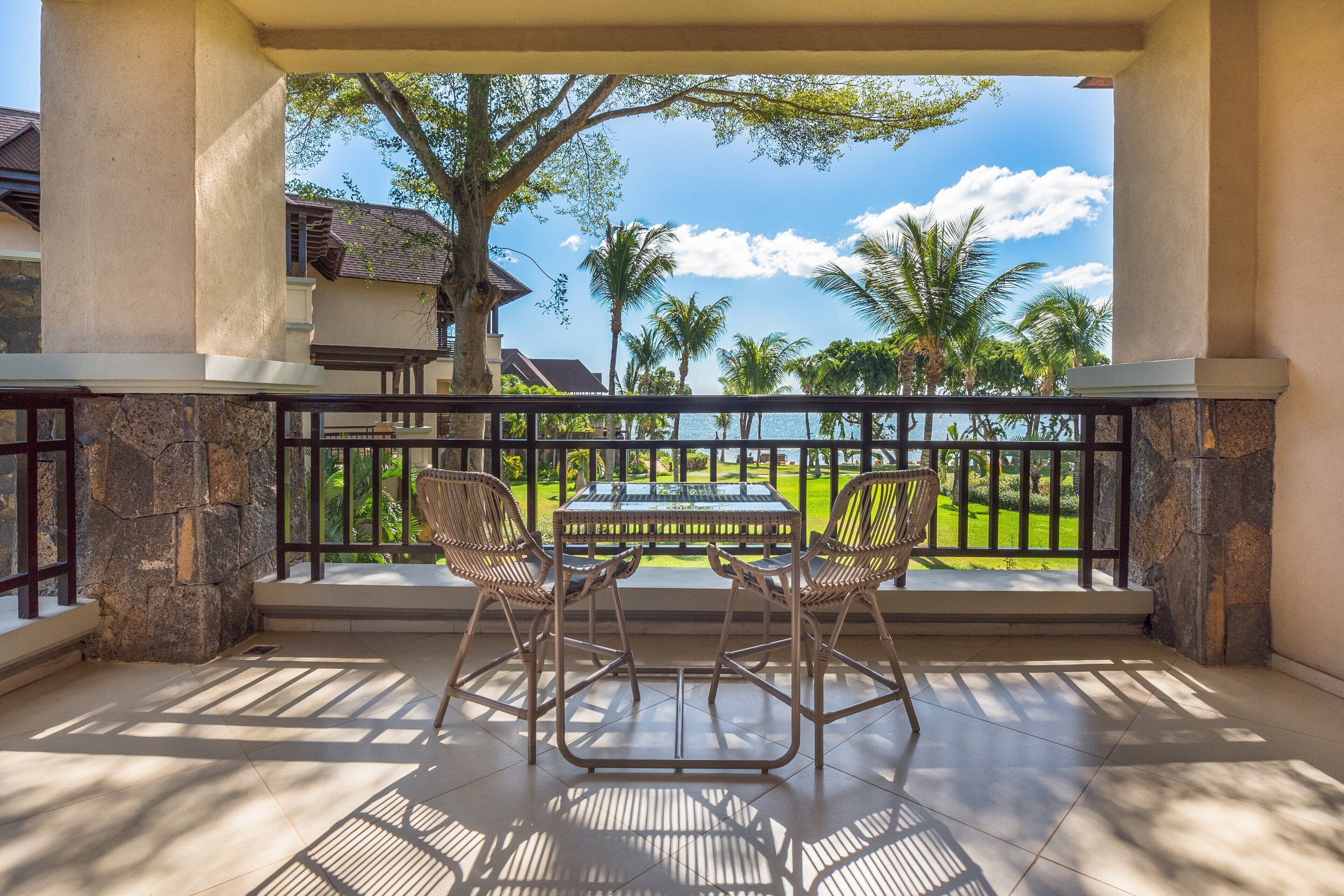 A balcony with a table and chairs, overlooking a lawn and palm trees.