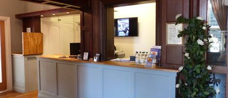 A reception desk with a television screen, a plant, and a sign indicating the Cedar Room.
