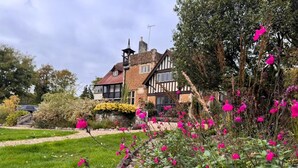A traditional Tudor-style house with a well-maintained garden featuring vibrant pink flowers. - Farnham House Hotel (Farnham)