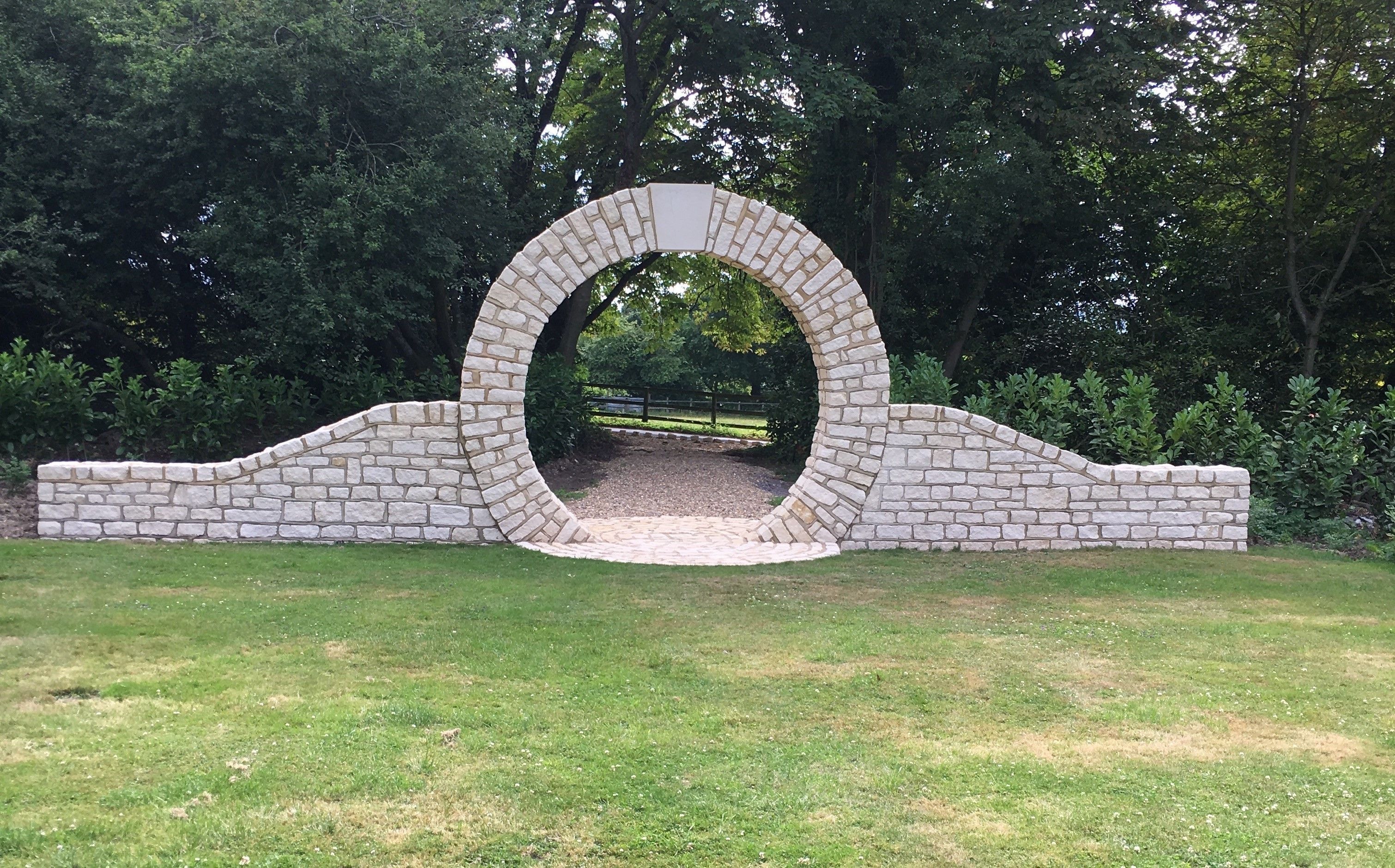 A stone archway in a park with a pathway leading through it.