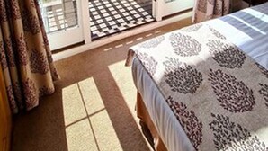 A bedroom with a bed, a window, and a sliding glass door leading to a balcony. - Farnham House Hotel (Farnham)