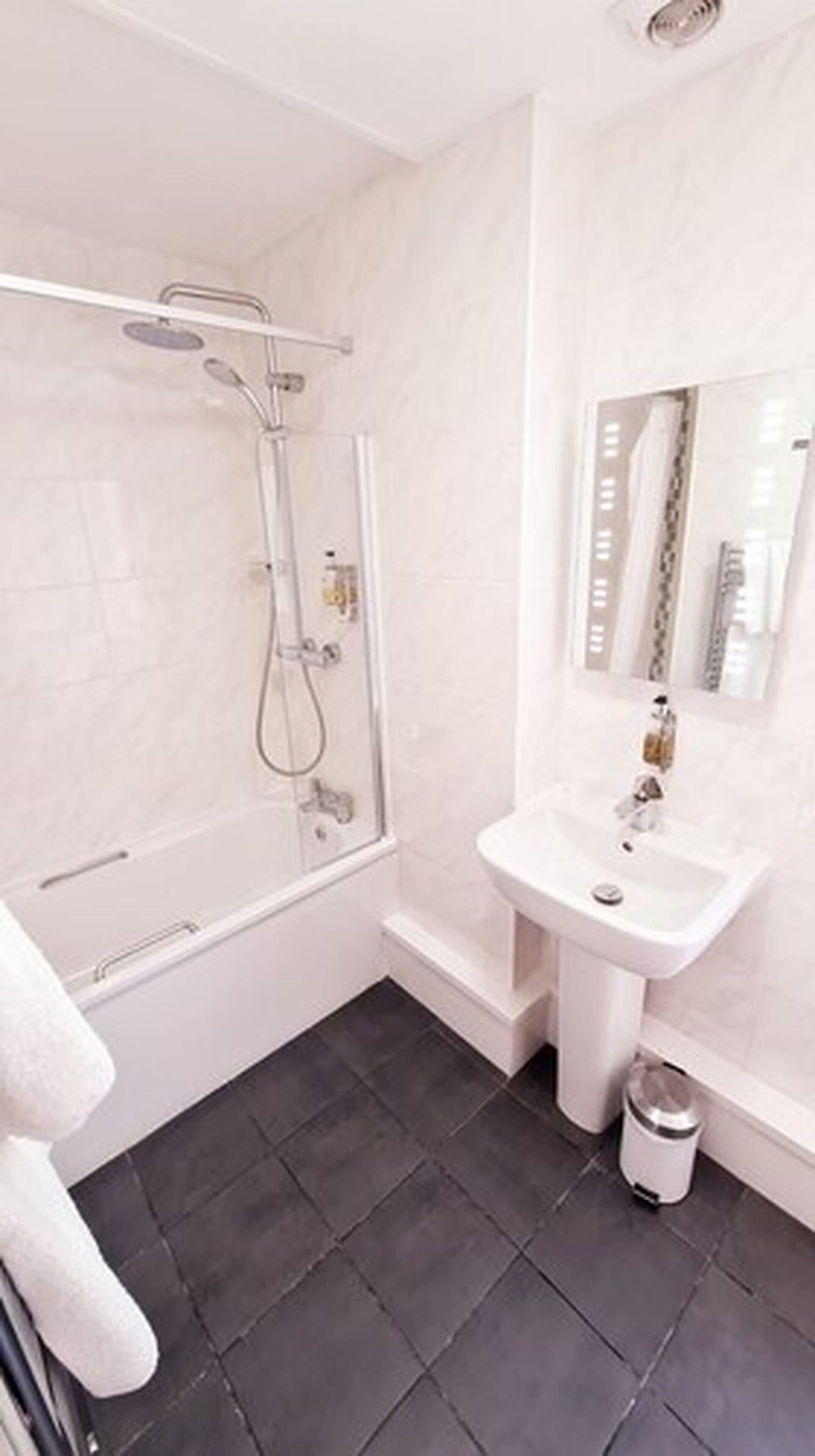 Un bany modern amb dutxa de vidre, un lavabo blanc i un mirall damunt.