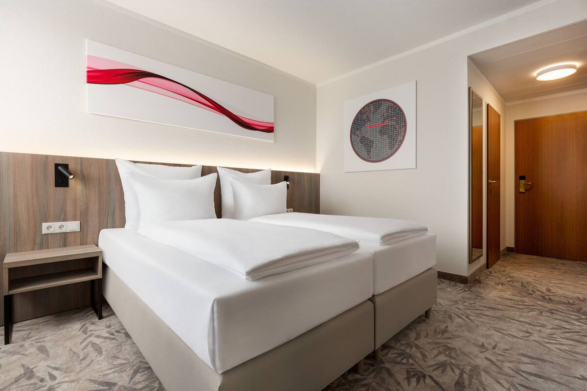 A modern hotel room with a large bed, a bedside table, and a wall-mounted artwork.