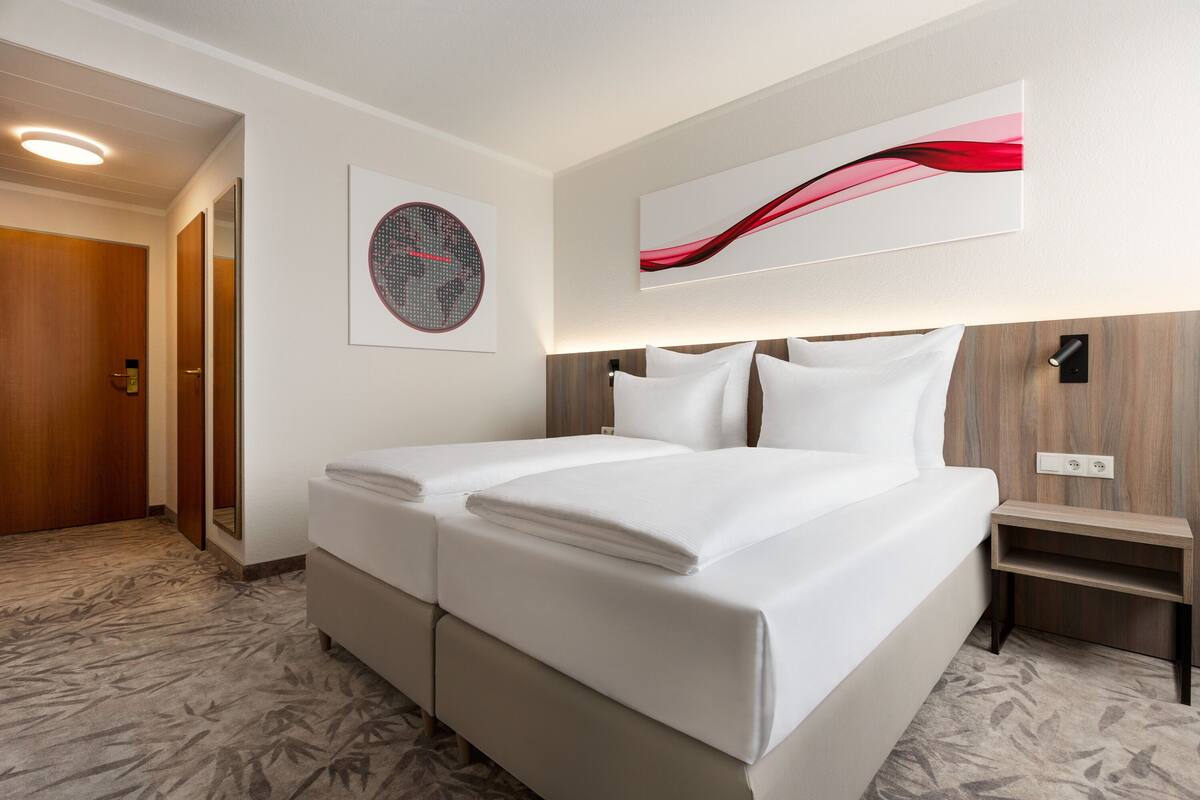 A hotel room with a double bed, a wooden headboard, a bedside table, and a wall-mounted light fixture.
