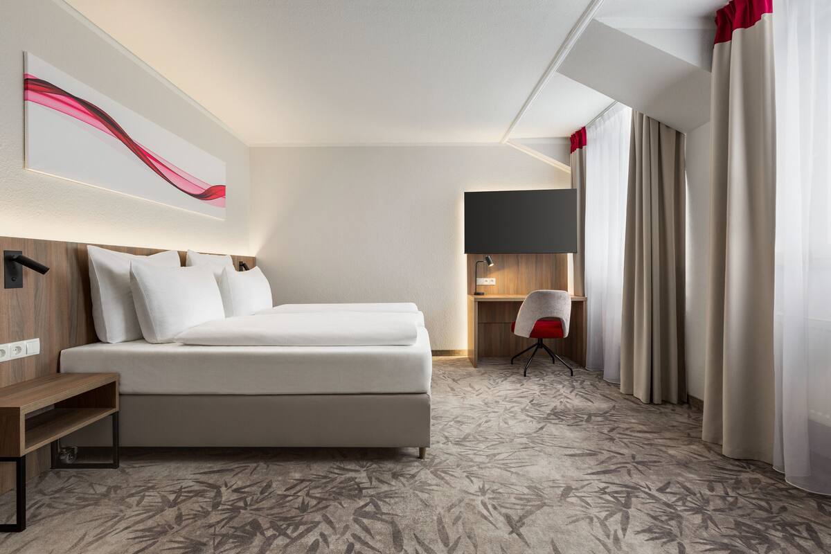 A modern hotel room with a large bed, a desk, and a chair.