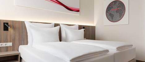 A neatly made bed with white linens, a wooden headboard, and a wall-mounted artwork above it.