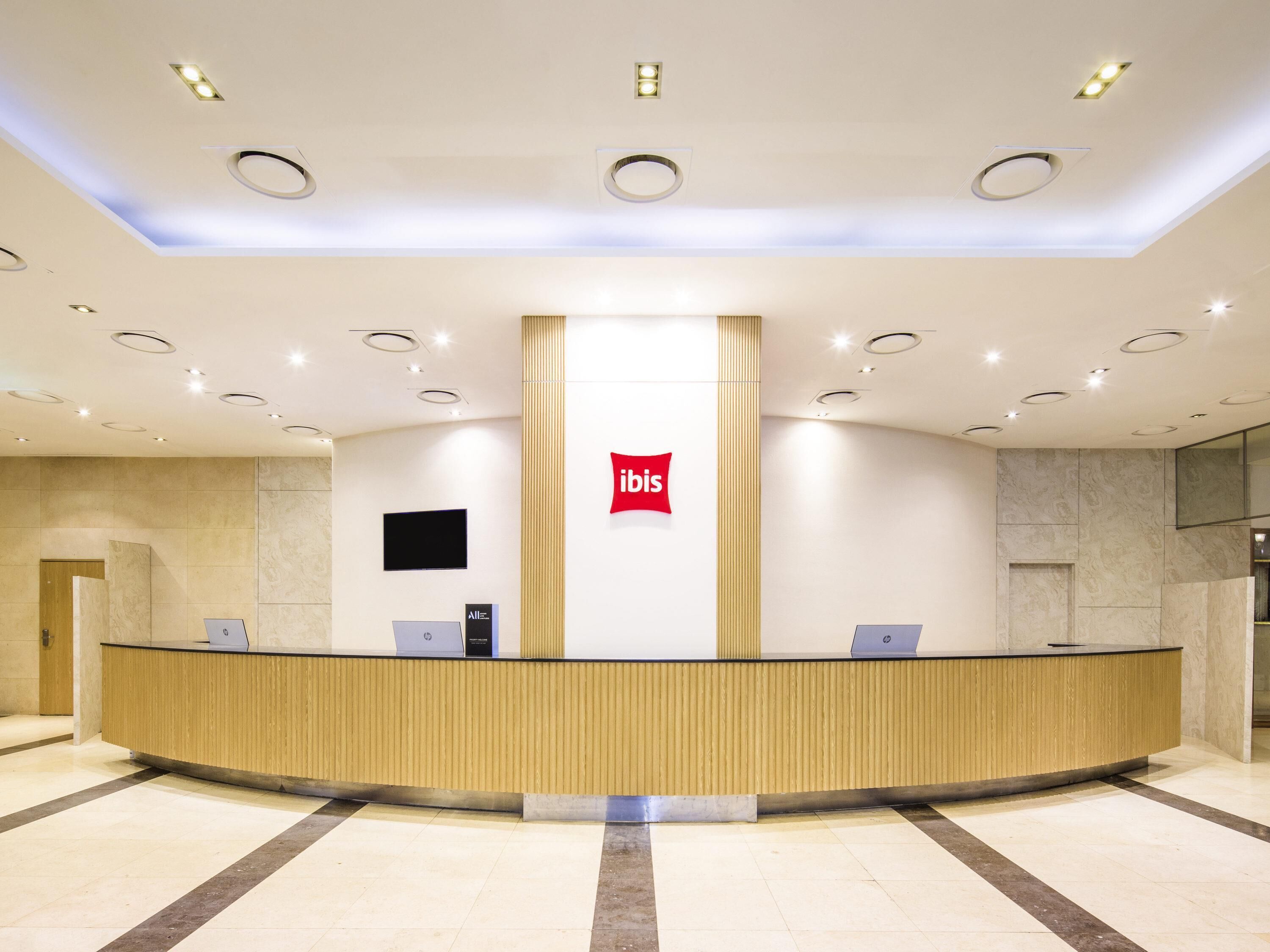 A hotel reception area with a central counter, a television mounted on the wall, and a logo above the counter.