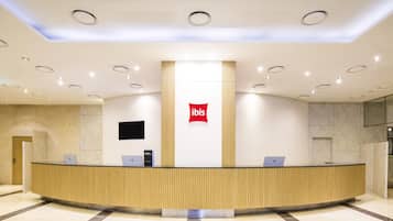 A hotel reception area with a central counter, a television mounted on the wall, and a logo above the counter.