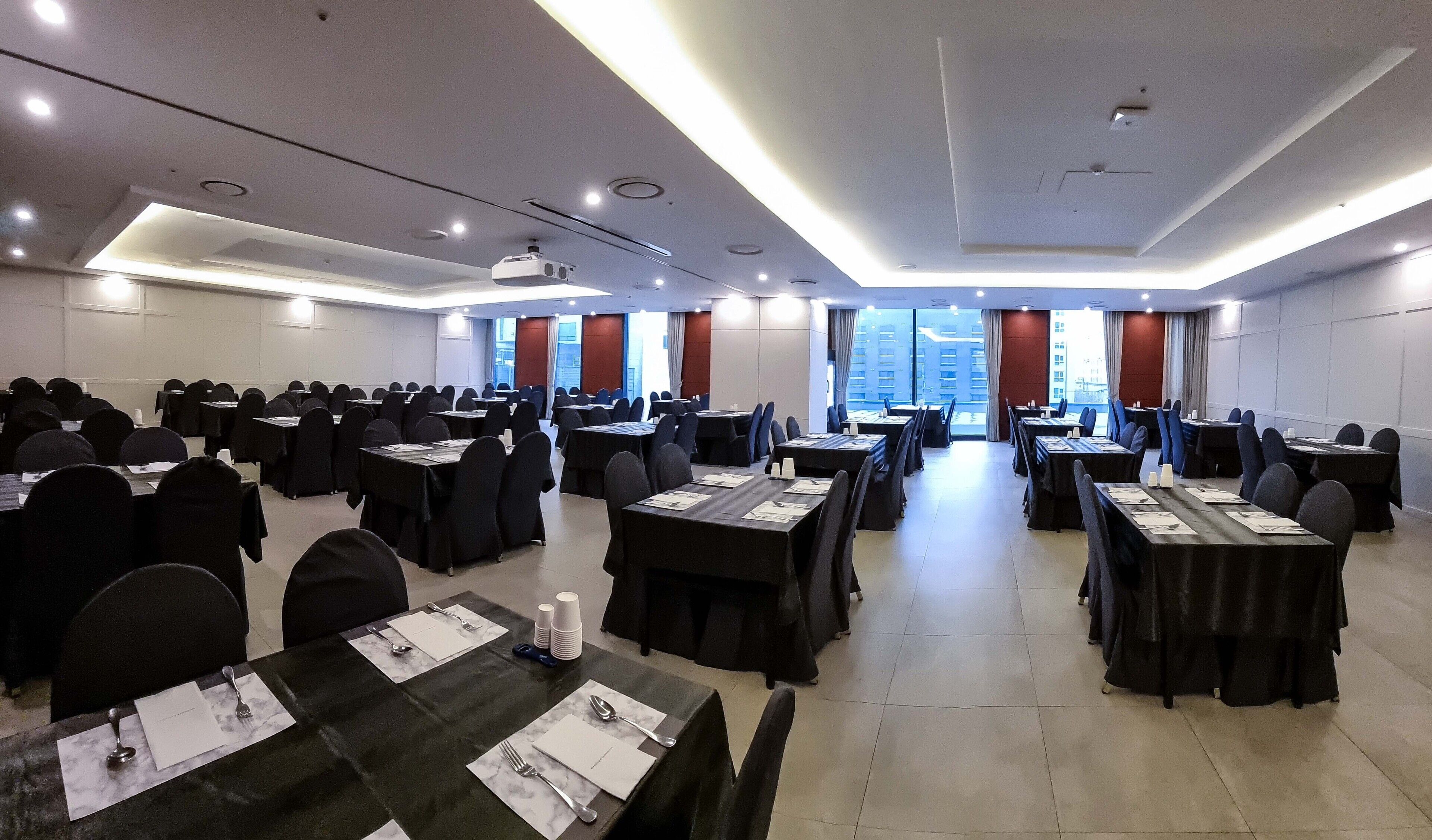 A conference room with multiple tables and chairs, equipped with nameplates and cutlery, and large windows with curtains.