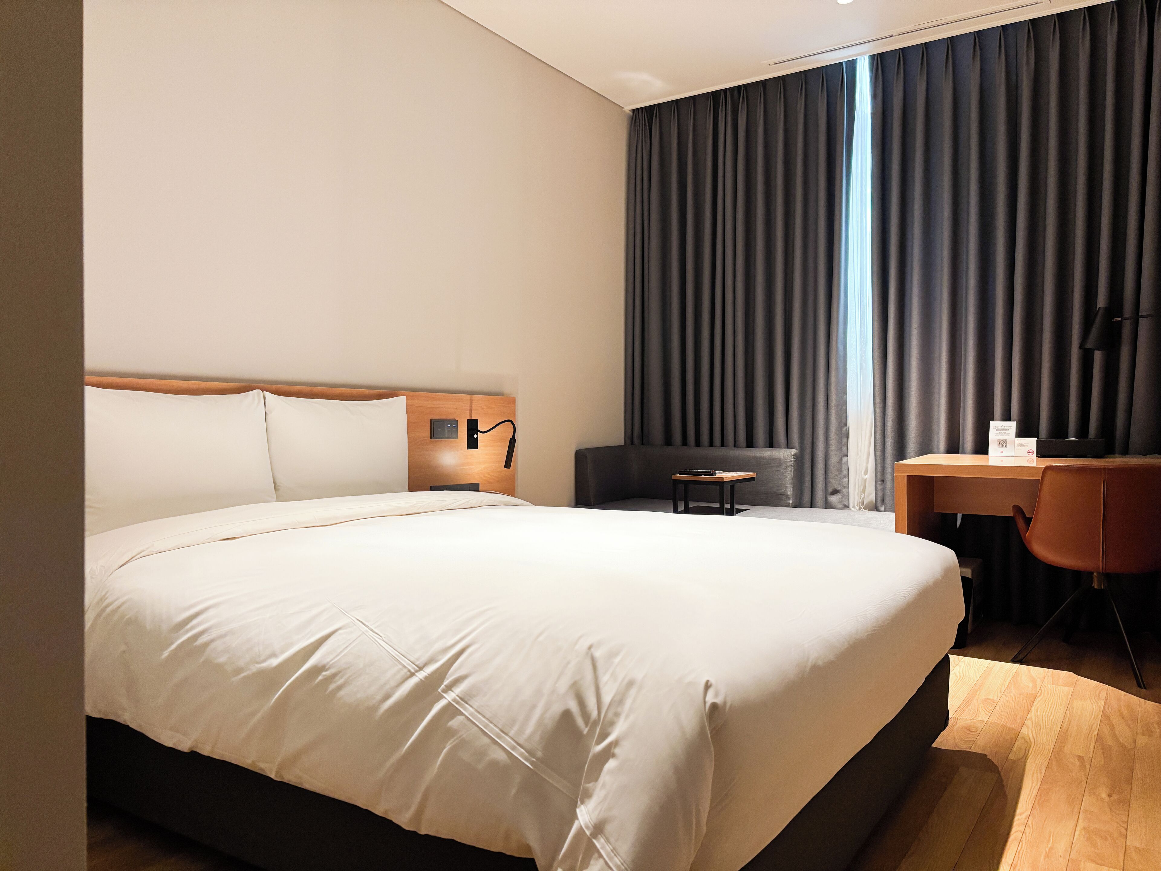 A hotel room with a large bed, a desk, a chair, and a window with curtains.