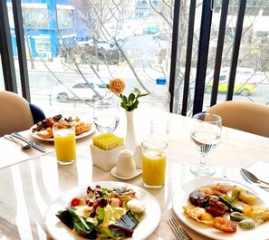 A dining table with plates of food, glasses of orange juice, and a vase with a single flower. - ibis Suwon Ambassador (Suwon)