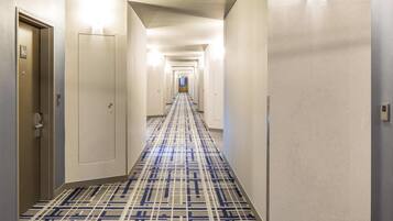 Ein Hotelgang mit Teppichmuster, Türen und einem beleuchteten Korridor.