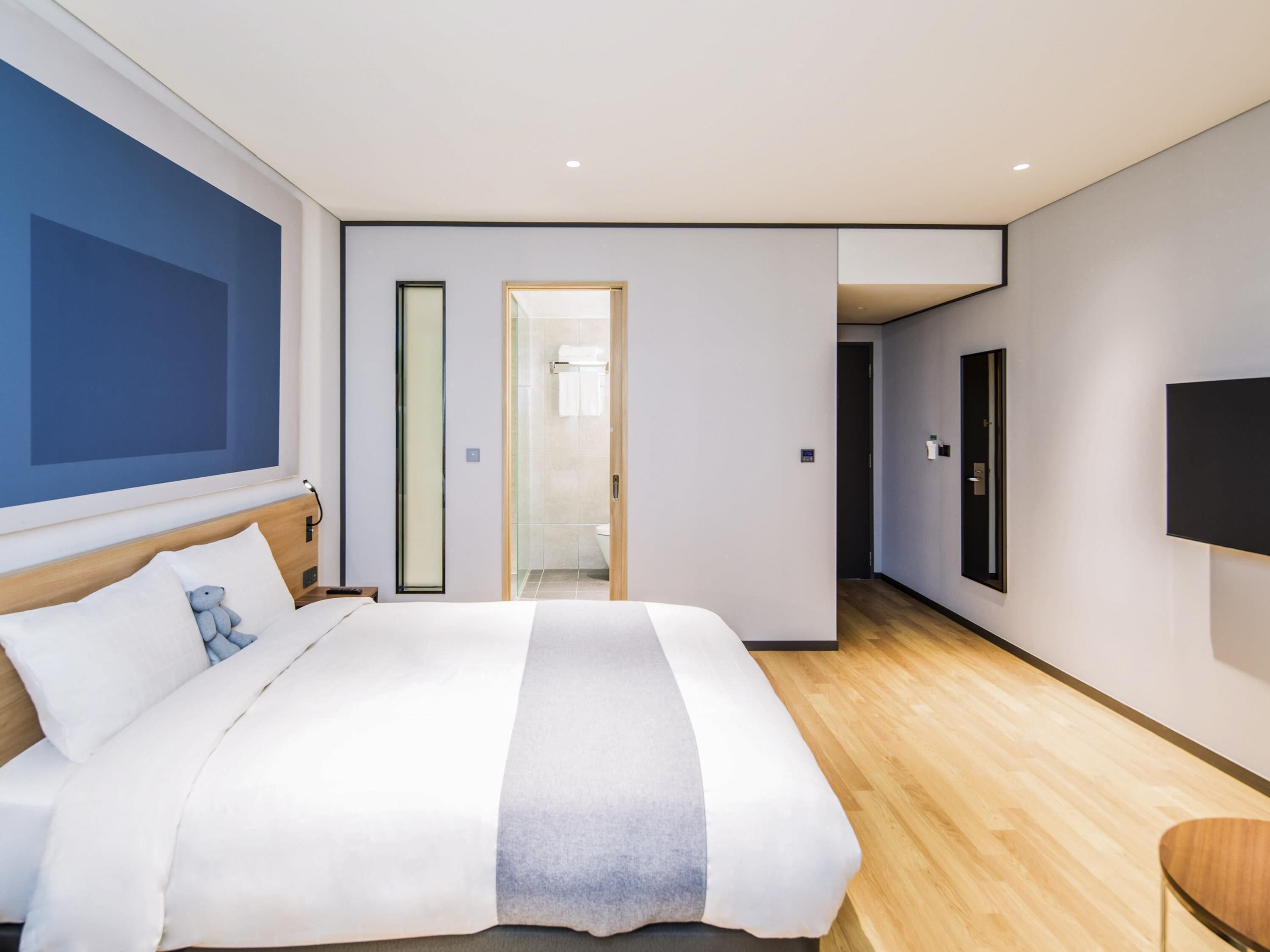 A modern hotel room with a large bed, a flat-screen TV, and a wooden floor.