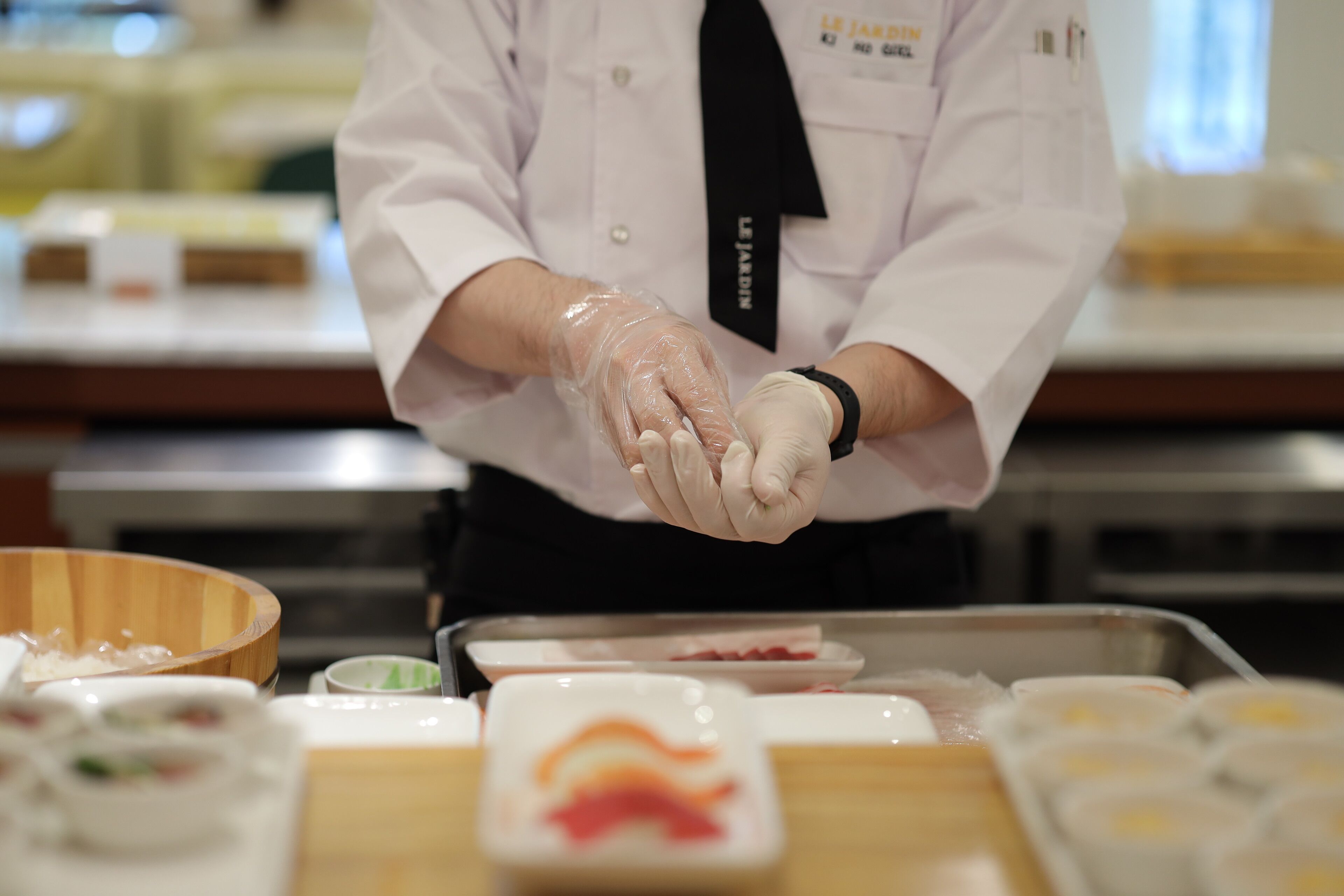 A person in a white uniform with a black tie, wearing gloves, handling food items on a counter.