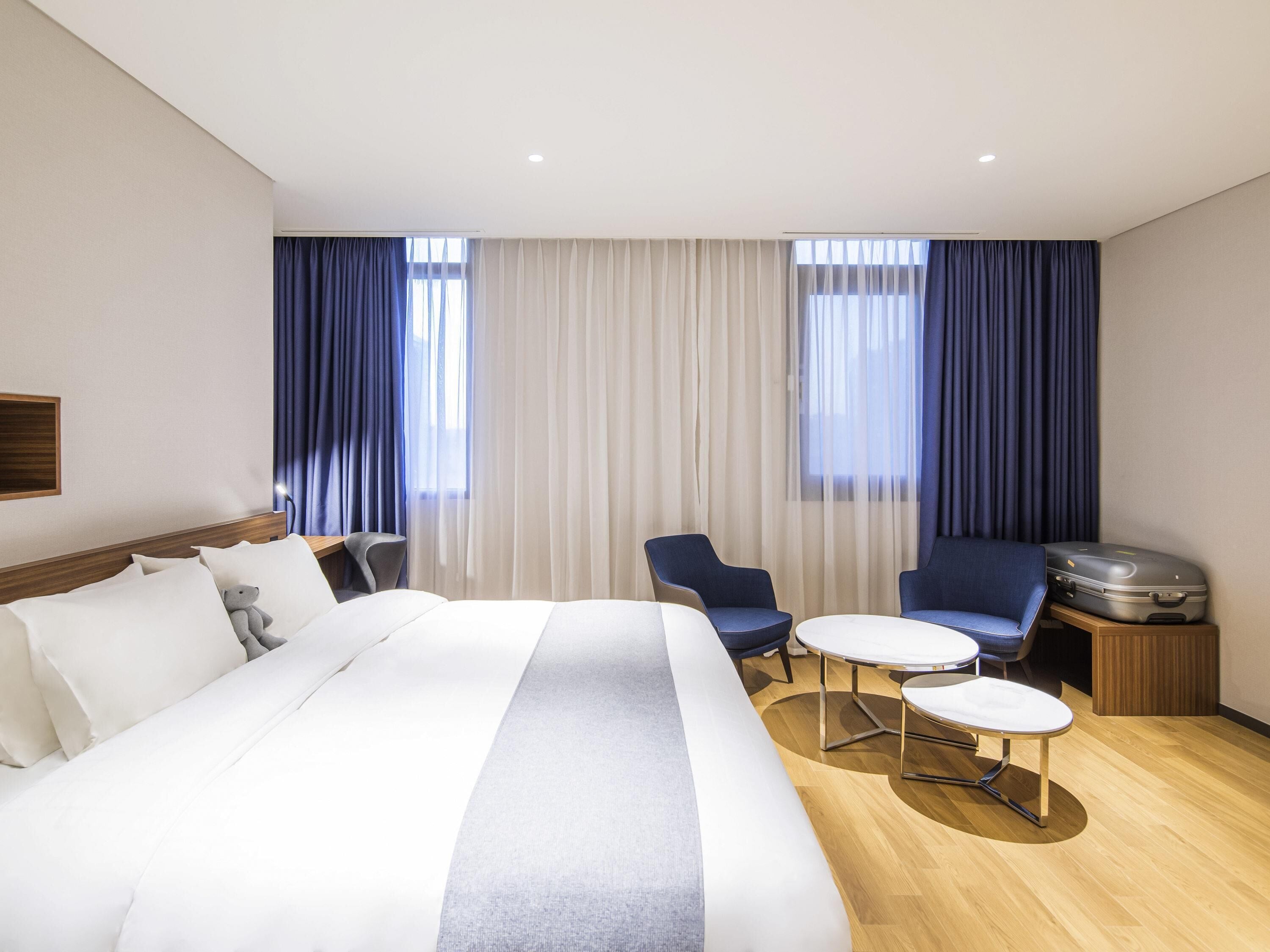 A hotel room with a large bed, two chairs, a small table, a TV, and curtains.