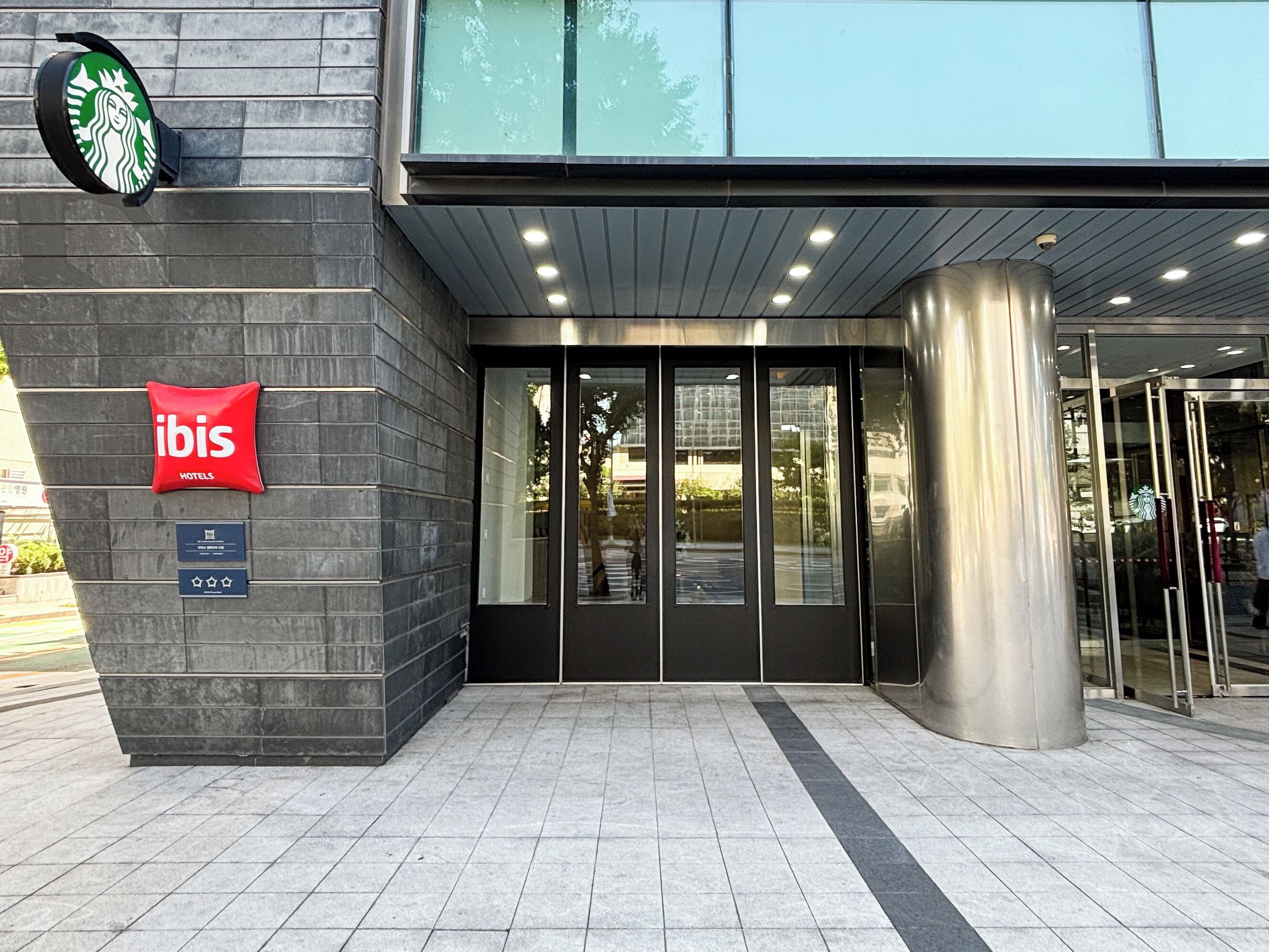 A hotel entrance with a glass door, a red 'ibis' sign, and a Starbucks logo above.