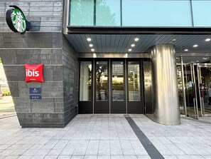 A hotel entrance with a glass door, a red 'ibis' sign, and a Starbucks logo above. - ibis Suwon Ambassador (Suwon)