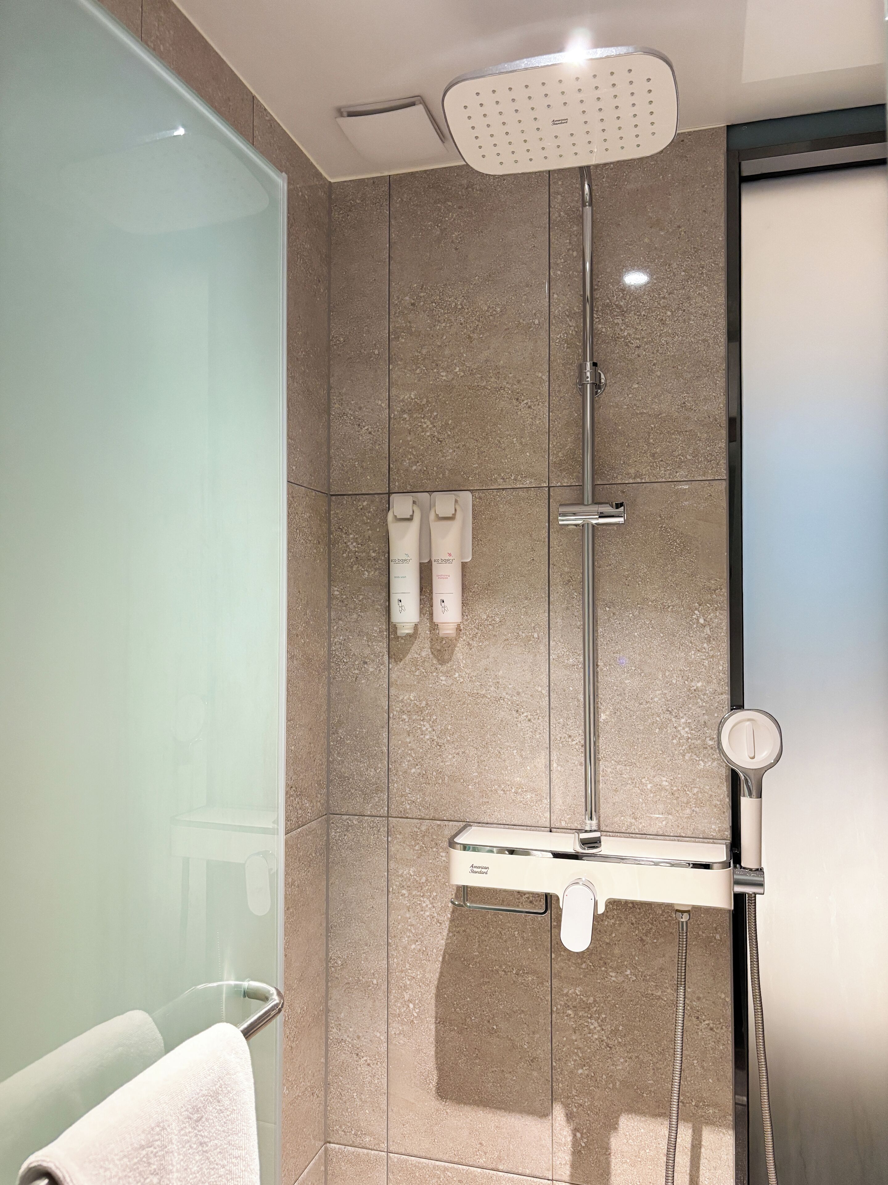 A modern bathroom with a glass shower enclosure, a handheld showerhead, and a built-in towel rack.