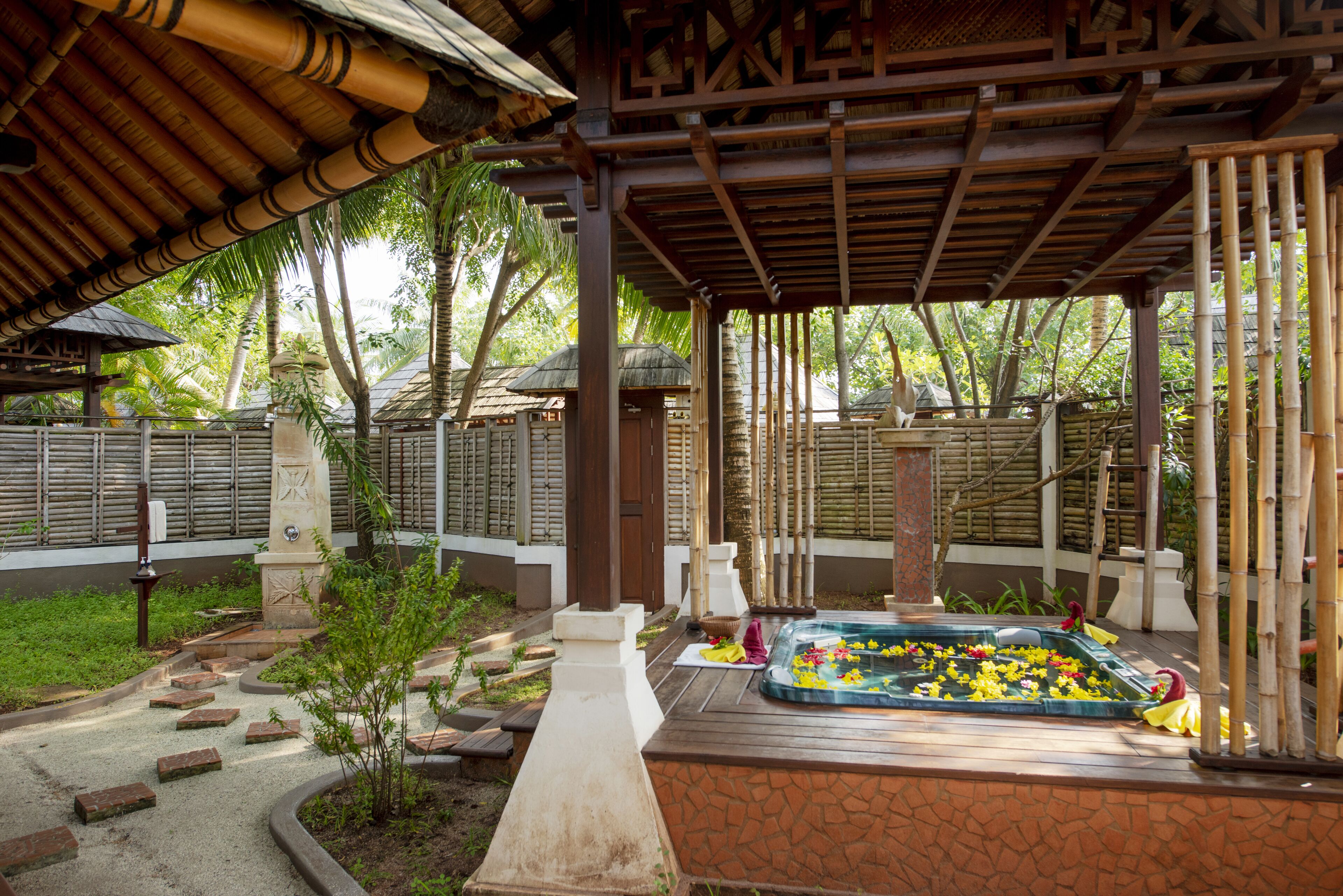 Un espace extérieur abrité, doté d’un jacuzzi entouré d’un jardin, de structures en bambou et d’un sentier en pierre.