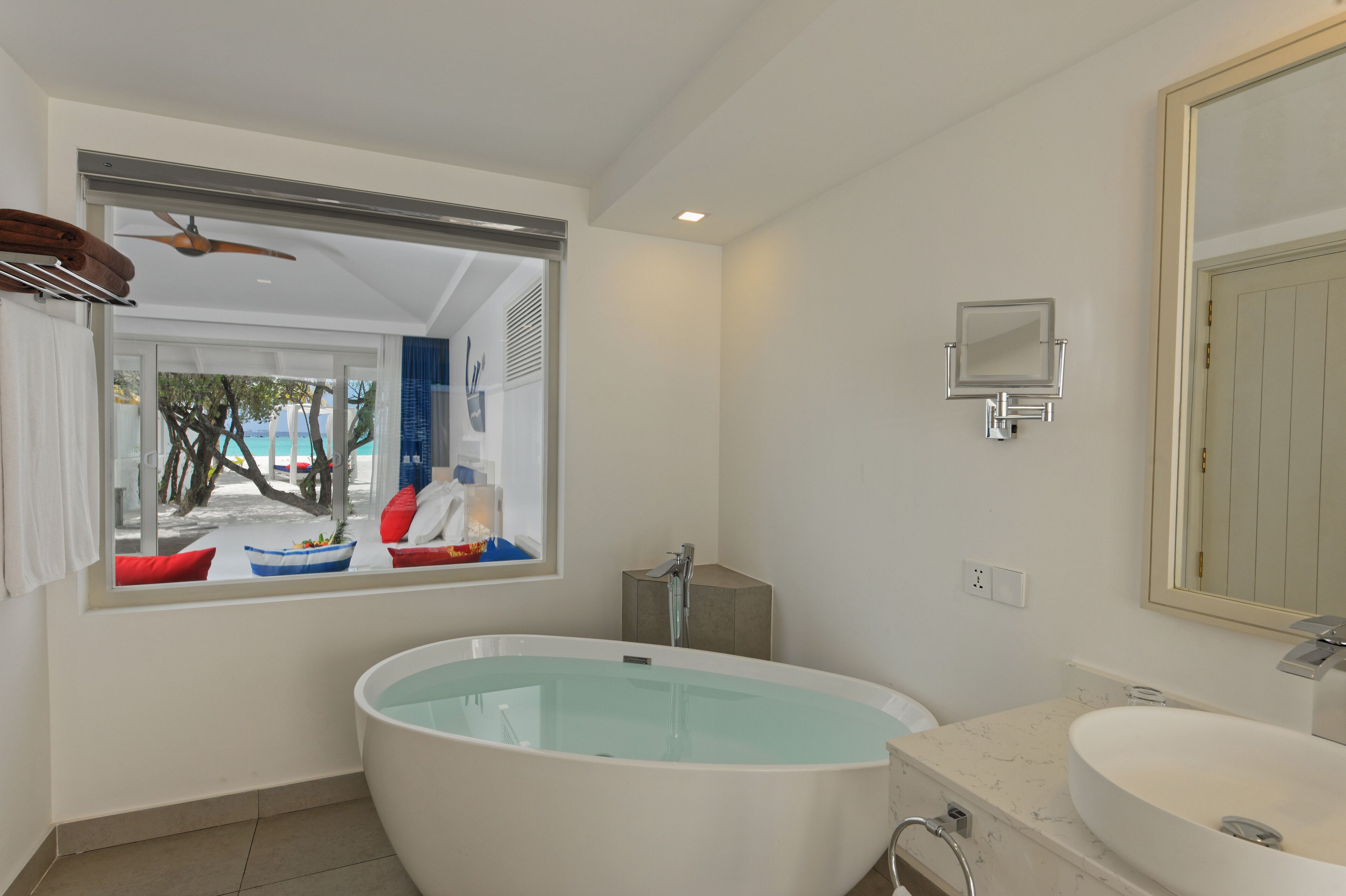 Un baño moderno con una bañera grande, un lavamanos y una ventana con vistas a la playa.