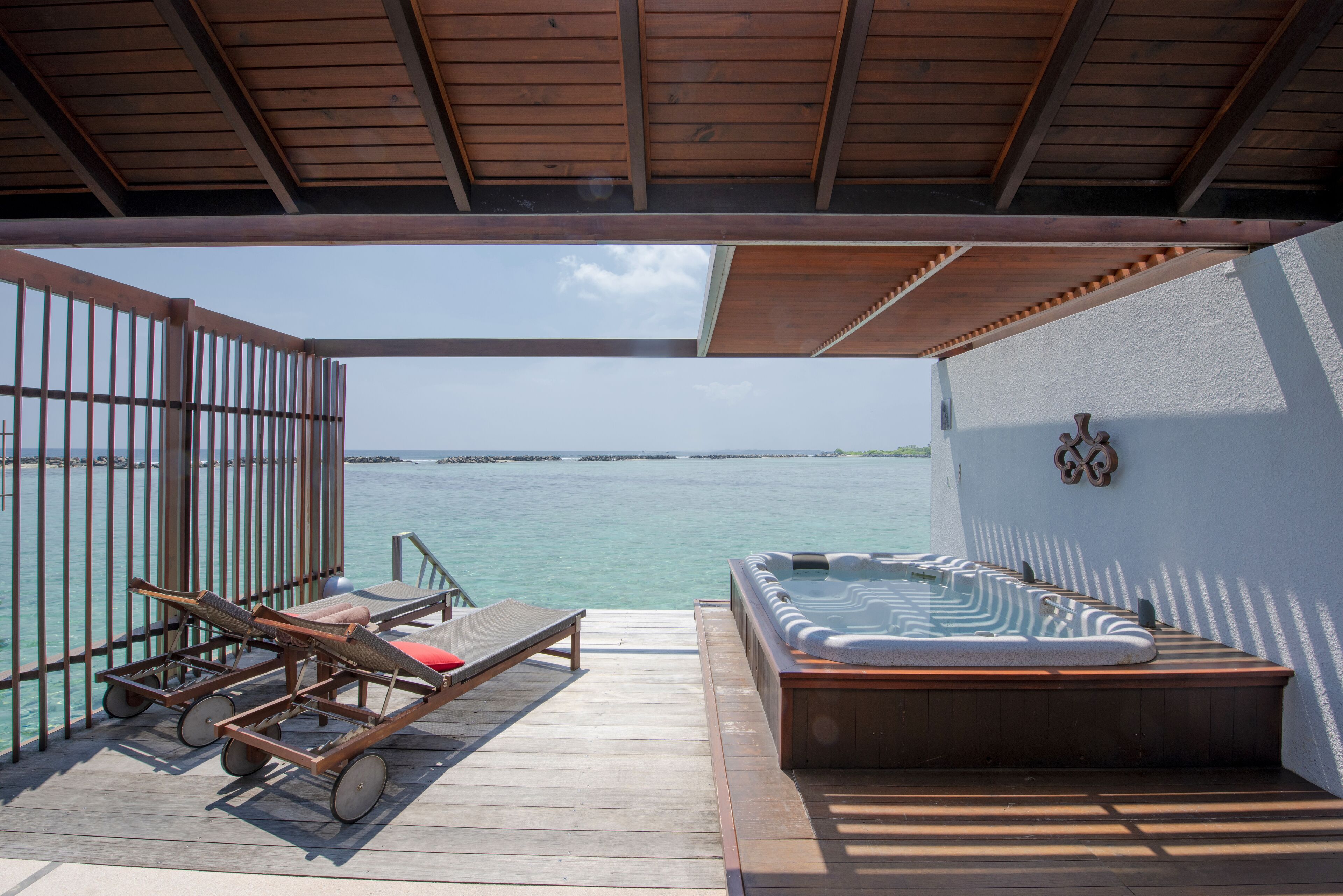 Une terrasse en bois avec un jacuzzi et des chaises longues donnant sur une étendue d’eau.