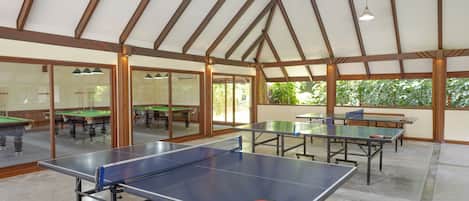An indoor recreational area with ping pong tables, a pool table, and a ceiling fan.