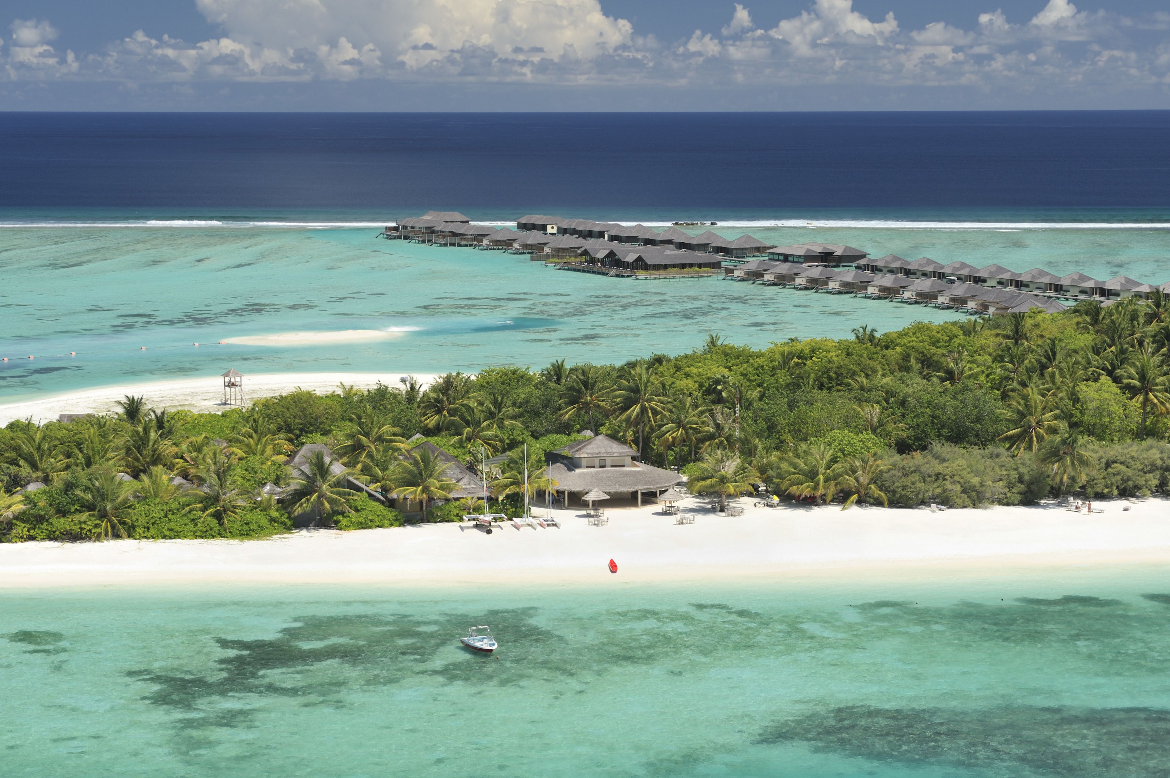 Een resort met bungalows op het water, diverse gebouwen, een strand en helder turquoise water.