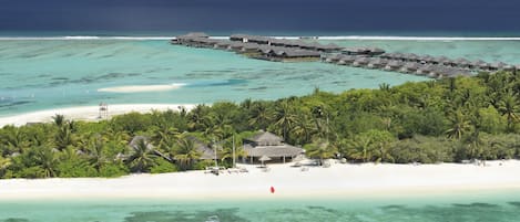 Een resort met bungalows op het water, diverse gebouwen, een strand en helder turquoise water.