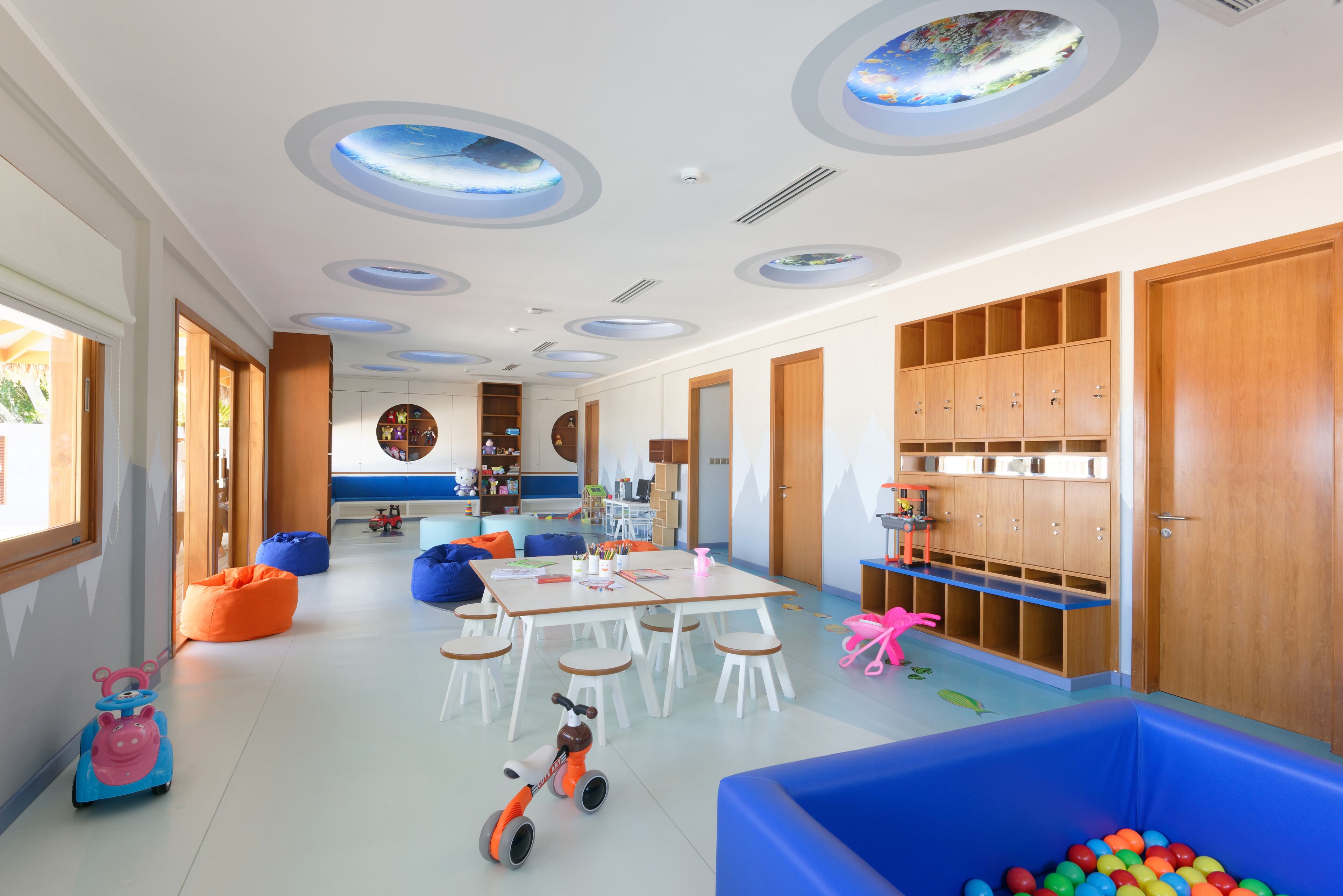 Una sala giochi per bambini con un tavolo grande, pouf e una piscina di palline.