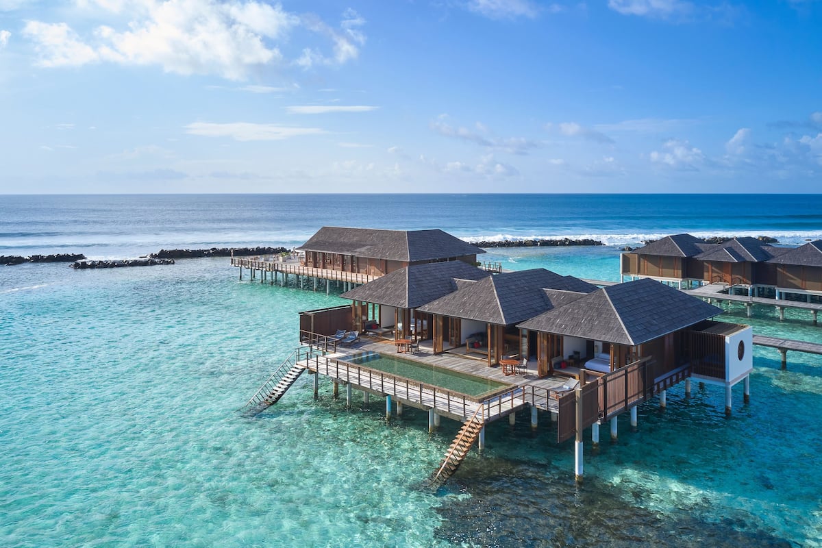 Bungalows sobre el agua con piscinas privadas, pasarelas de madera y vistas al océano.