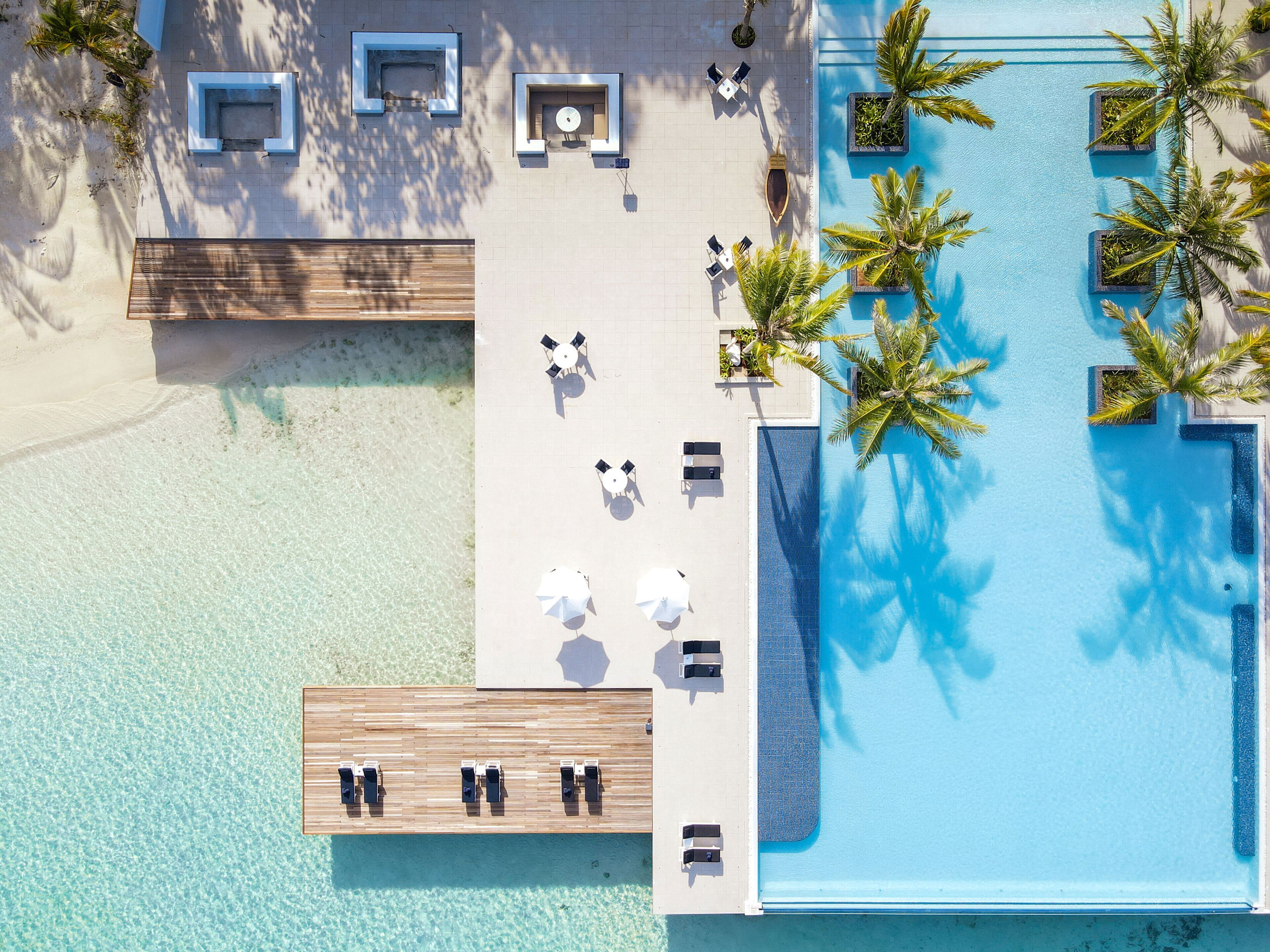 Vue aérienne d’un complexe hôtelier avec une piscine, des chaises longues et des palmiers.