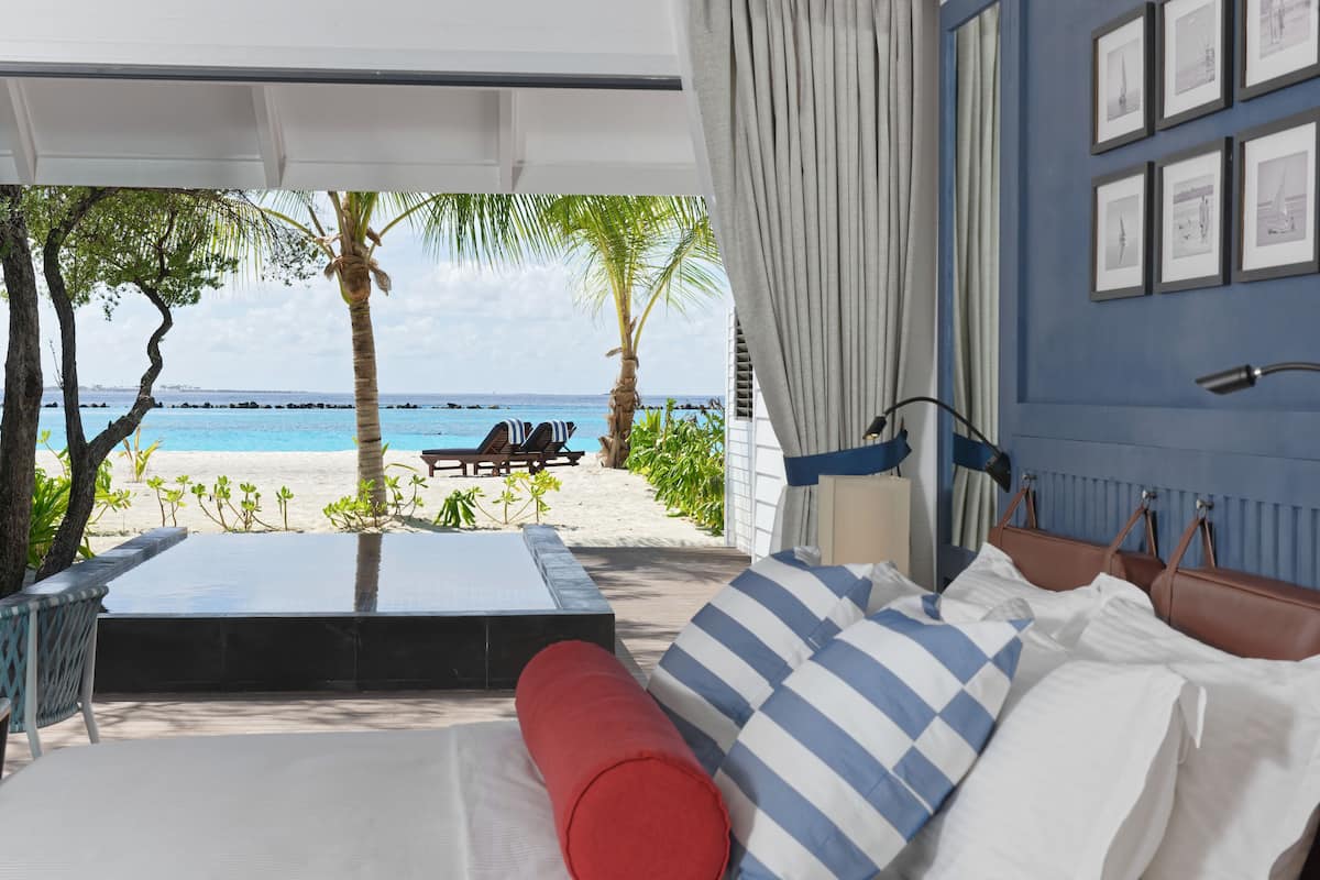 Una habitación con vista a la playa, una cama con almohadillas a rayas, una almohada roja y una mesa de madera.