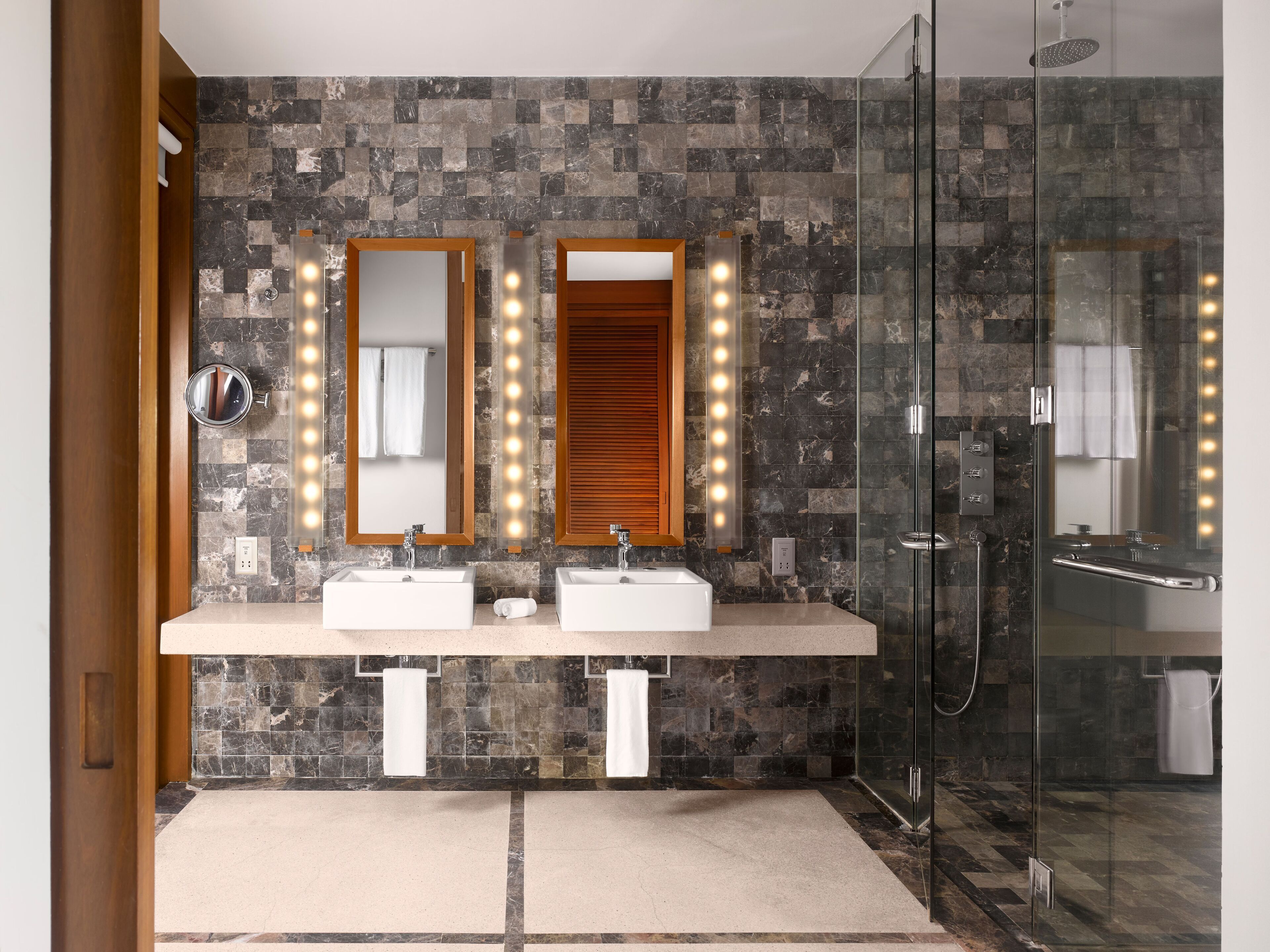 A modern bathroom with two sinks, a glass shower enclosure, and a vanity mirror with lights.