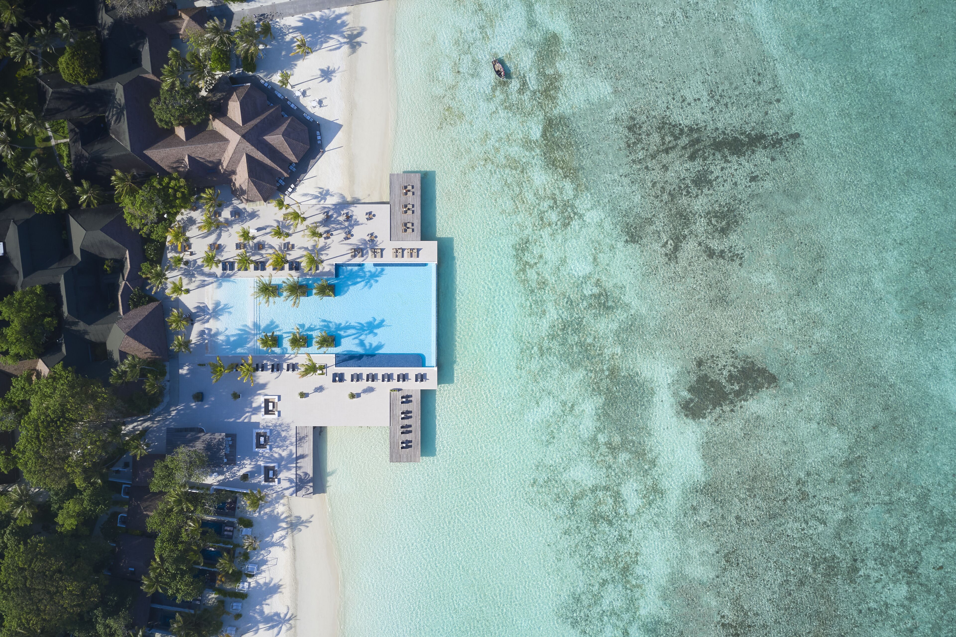 An aerial view of a resort with a swimming pool, beach, and palm trees.