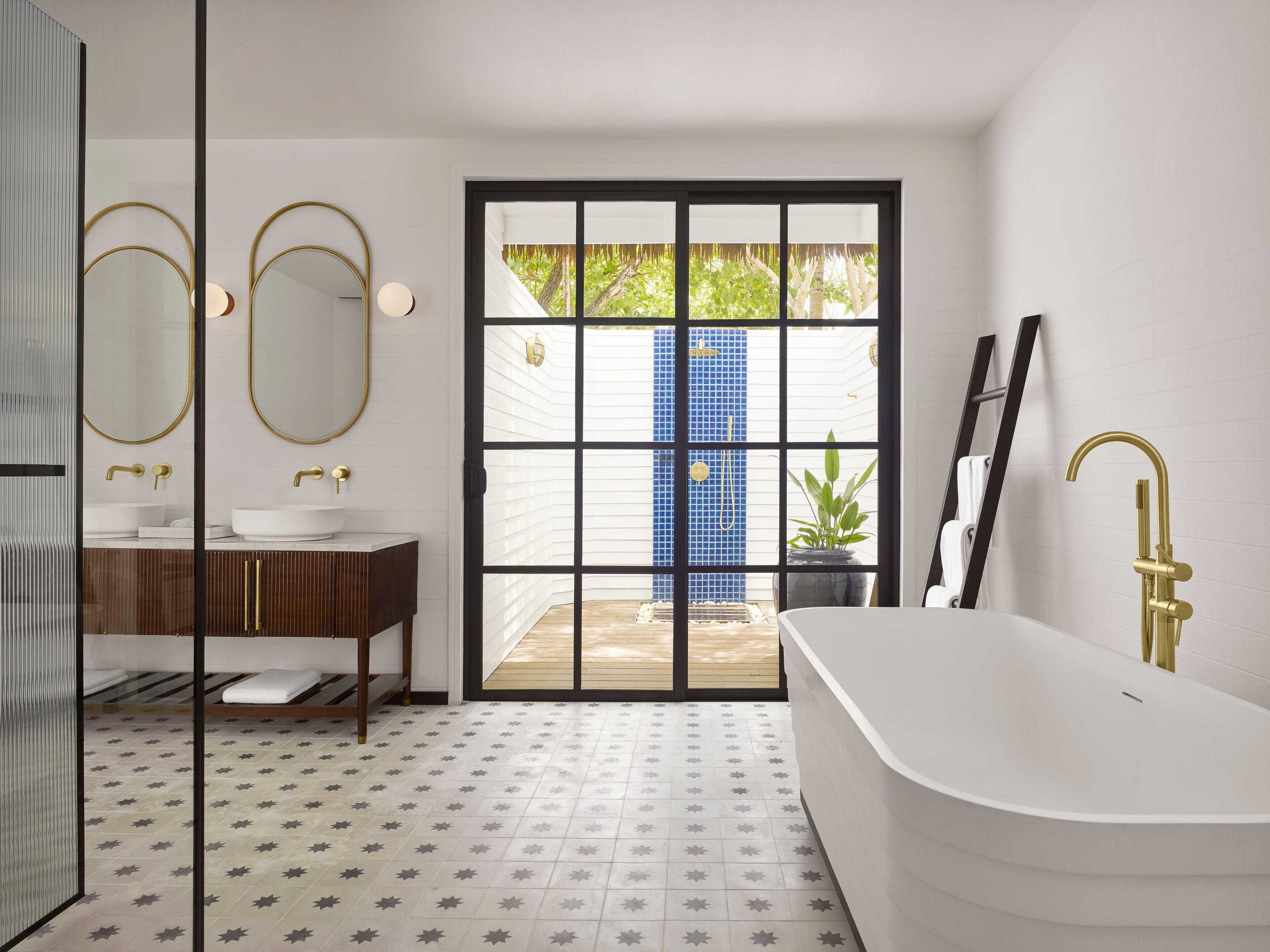 A modern bathroom with a freestanding bathtub, a vanity with gold fixtures, and a large mirror.