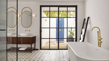 A modern bathroom with a freestanding bathtub, a vanity with gold fixtures, and a large mirror.