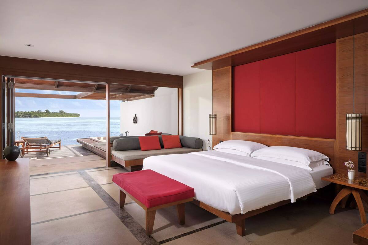 Un dormitorio con una cama grande, un banco, un sofá y vistas al océano.