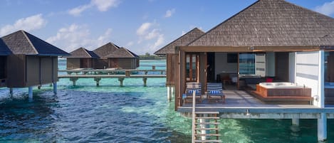 Overwater bungalows with clear blue water, wooden decks, and a hot tub.