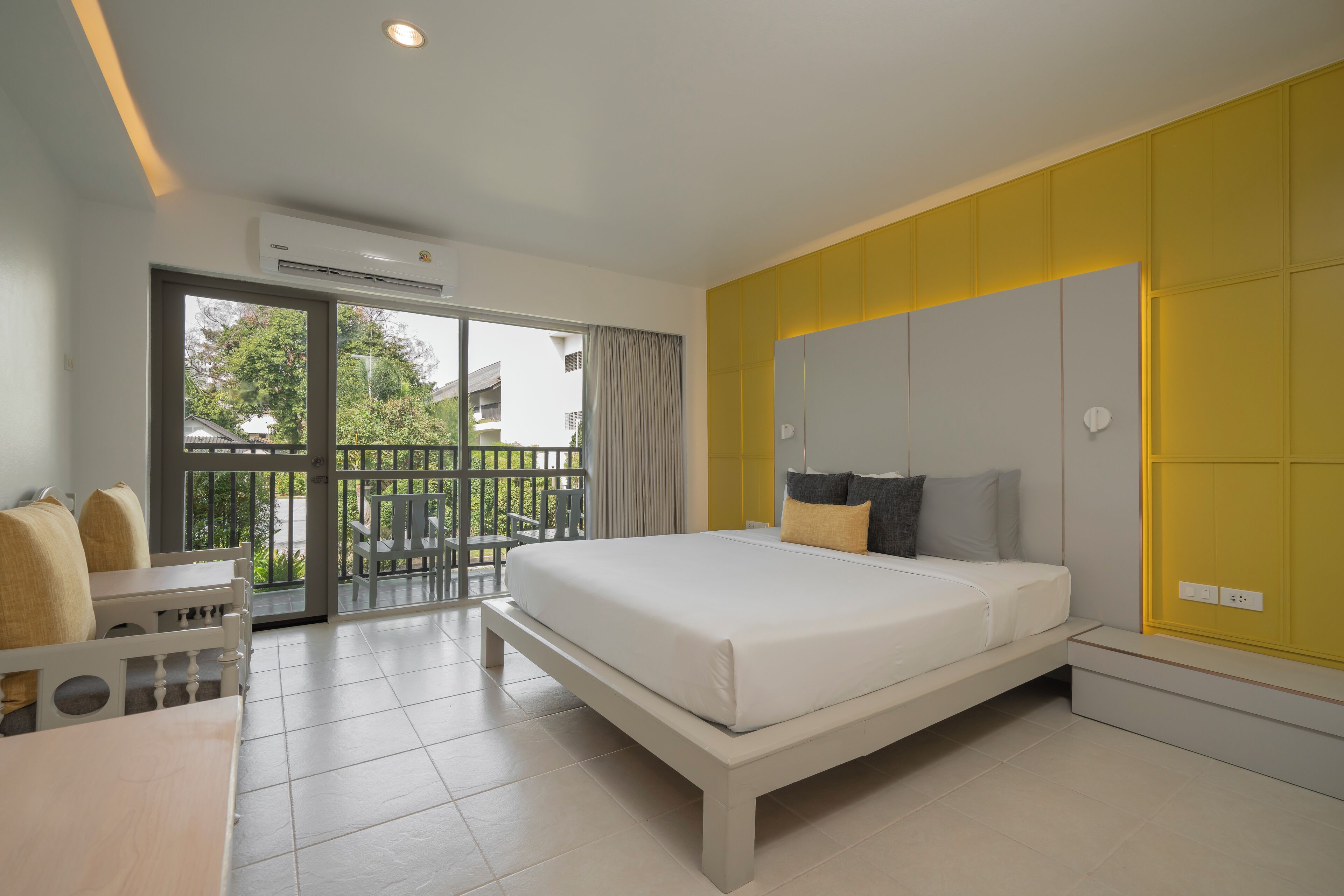 A modern bedroom with a large bed, a balcony with a view, and a yellow accent wall.