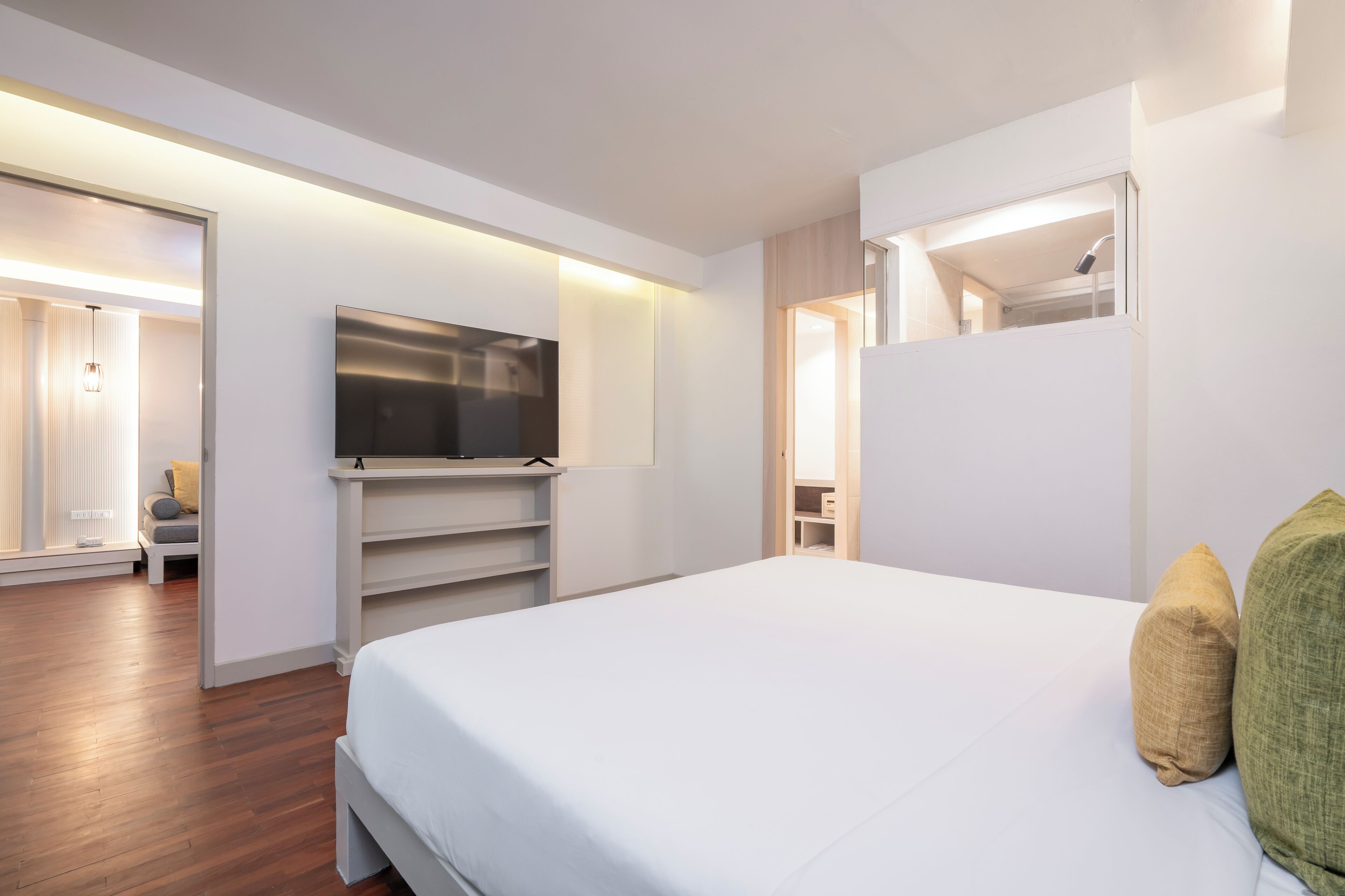 A modern hotel room with a large bed, a flat-screen TV mounted on the wall, a walk-in closet, and a bathroom visible through an open door.