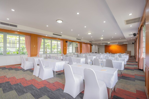 A conference room with multiple tables and chairs, large windows with curtains, and a carpeted floor. - Sunshine Garden Resort (Pattaya)
