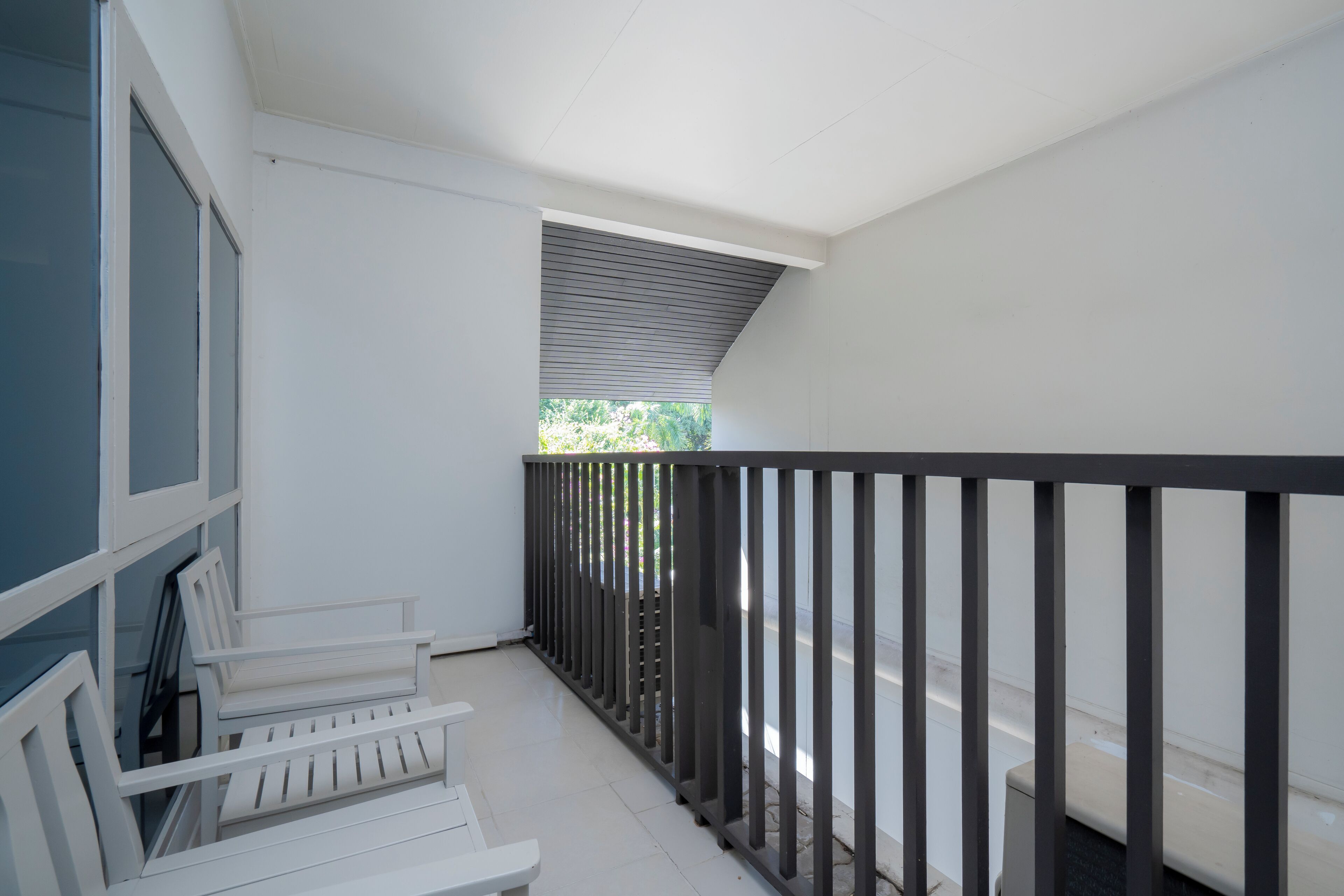 A balcony with a white railing, a white bench, and a view of greenery outside.
