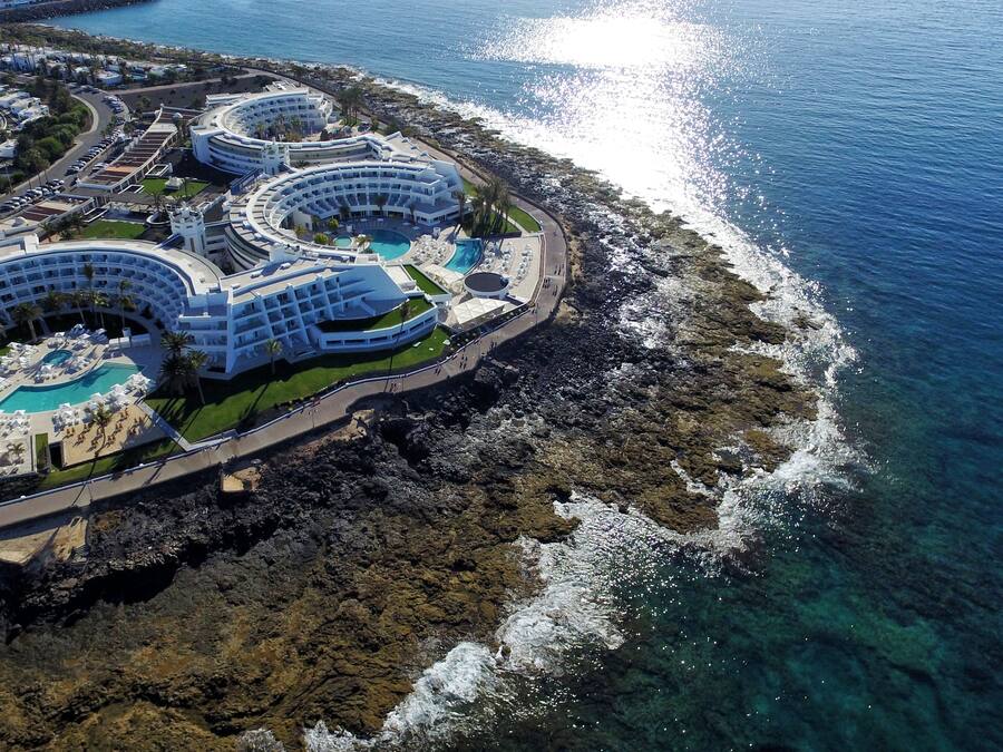 An aerial view of a resort with multiple circular buildings, a central pool, and a rocky coastline.