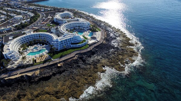 An aerial view of a resort with multiple circular buildings, a central pool, and a rocky coastline. - Iberostar Selection Lanzarote Park (Yaiza)