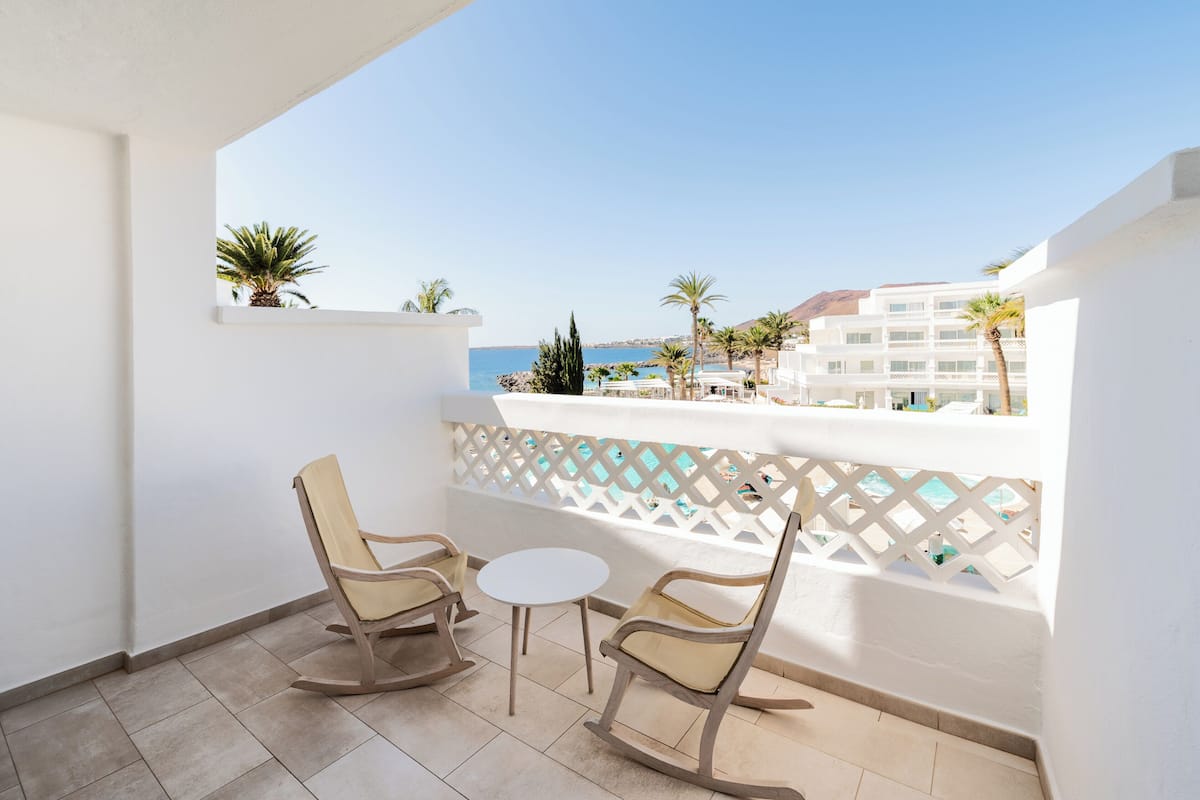 Un balcón con dos mecedoras y una mesita, con vista a una piscina y edificios.