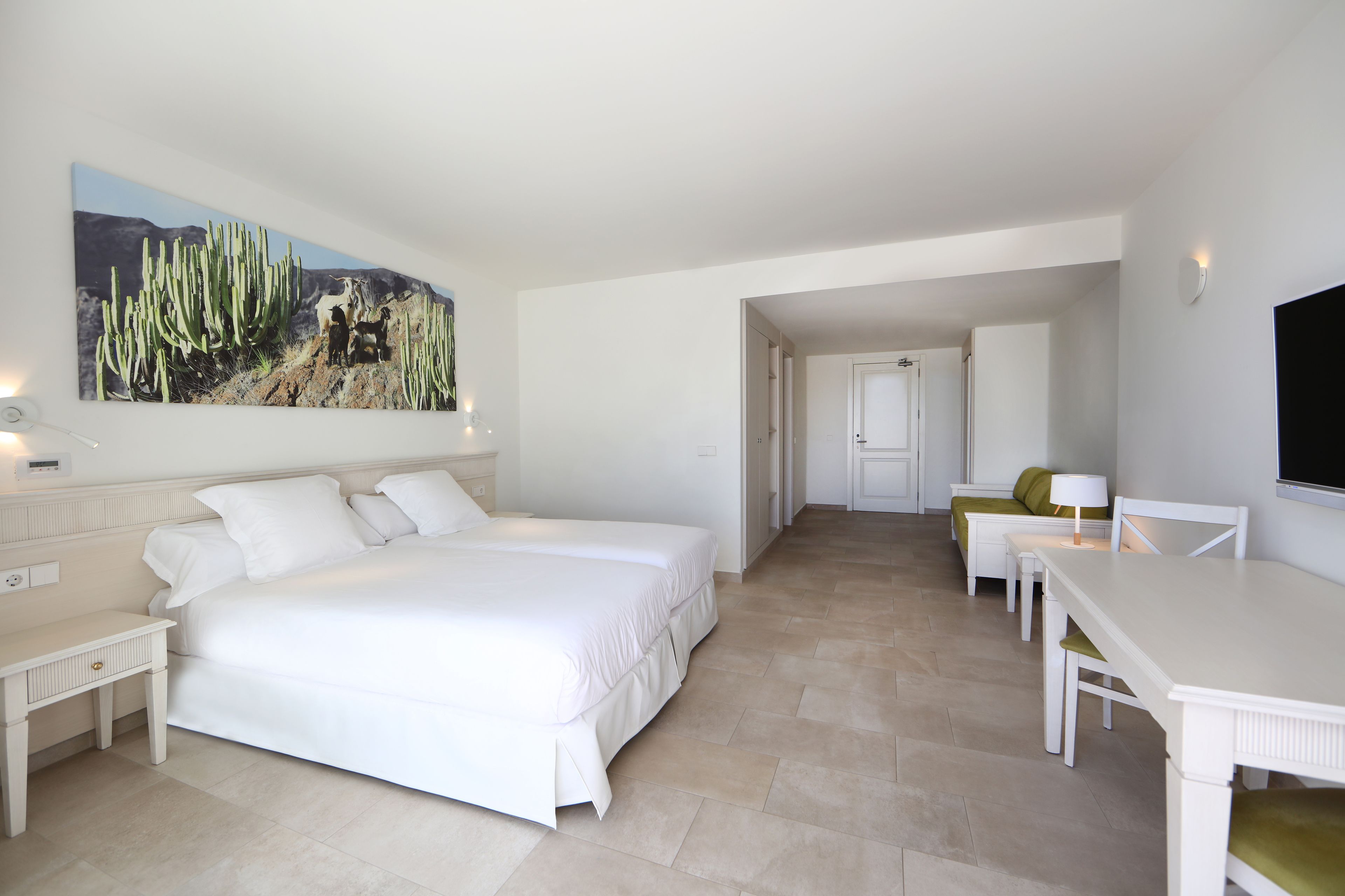 Un dormitorio con una cama grande, un escritorio y una silla. Hay un cuadro en la pared y una puerta que da a otra habitación.